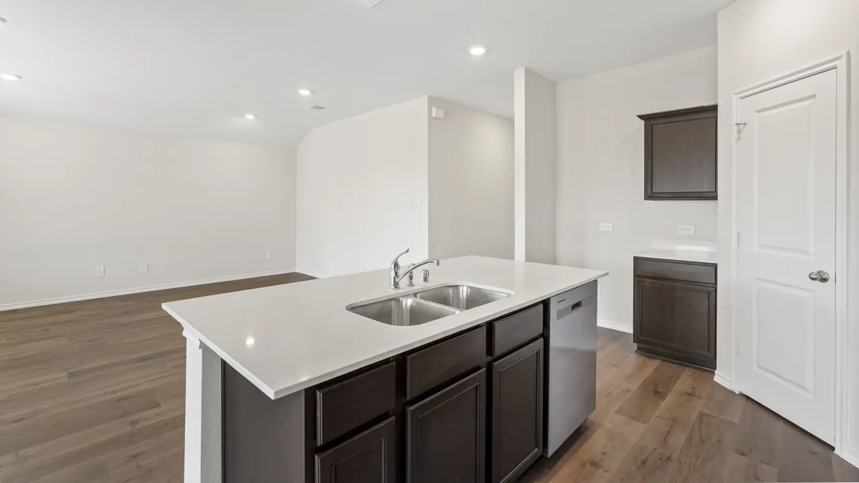 Kitchen island featuring a double basin sink with a chrome faucet, light-toned countertop, dark wood-finish cabinetry, and a stainless steel dishwasher