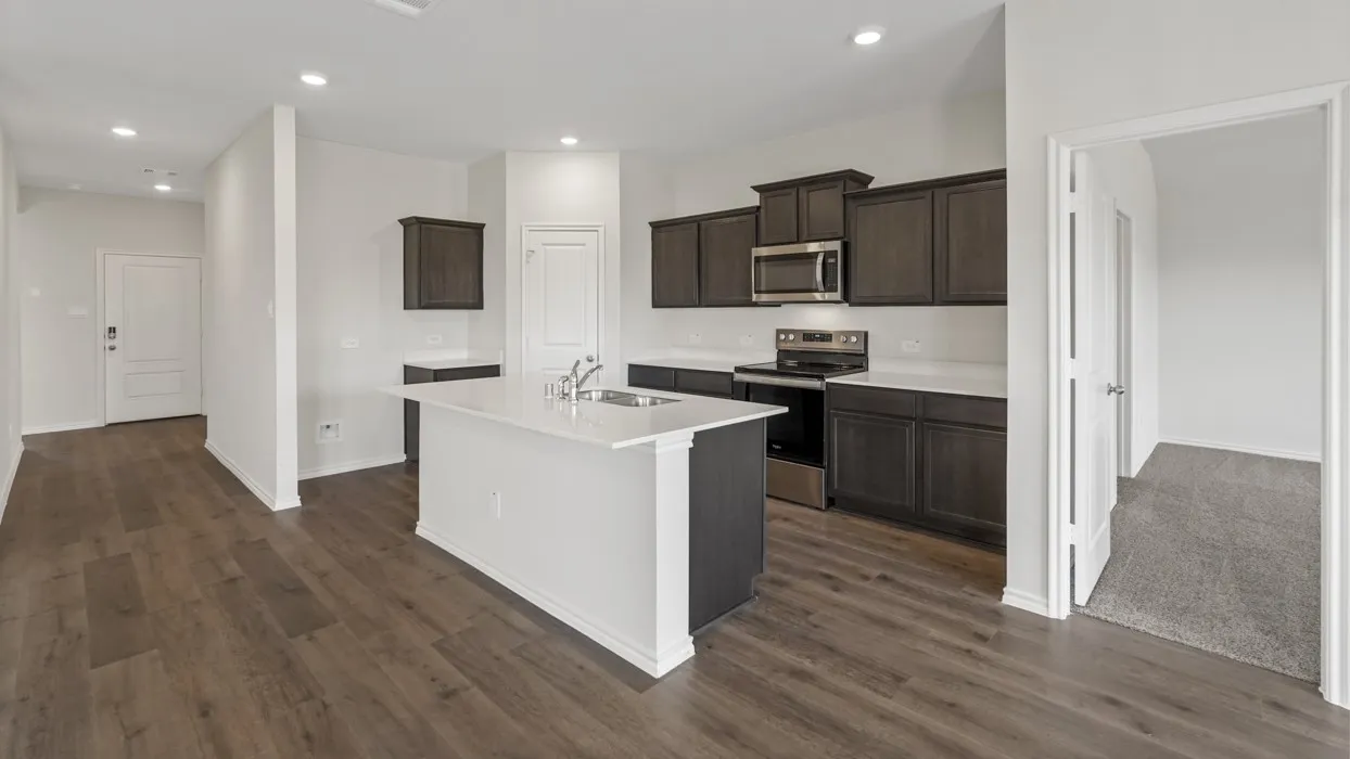 Modern kitchen featuring a central island with a sink, dark wood-finish cabinetry, stainless steel appliances, white countertops, and wood-finish flooring