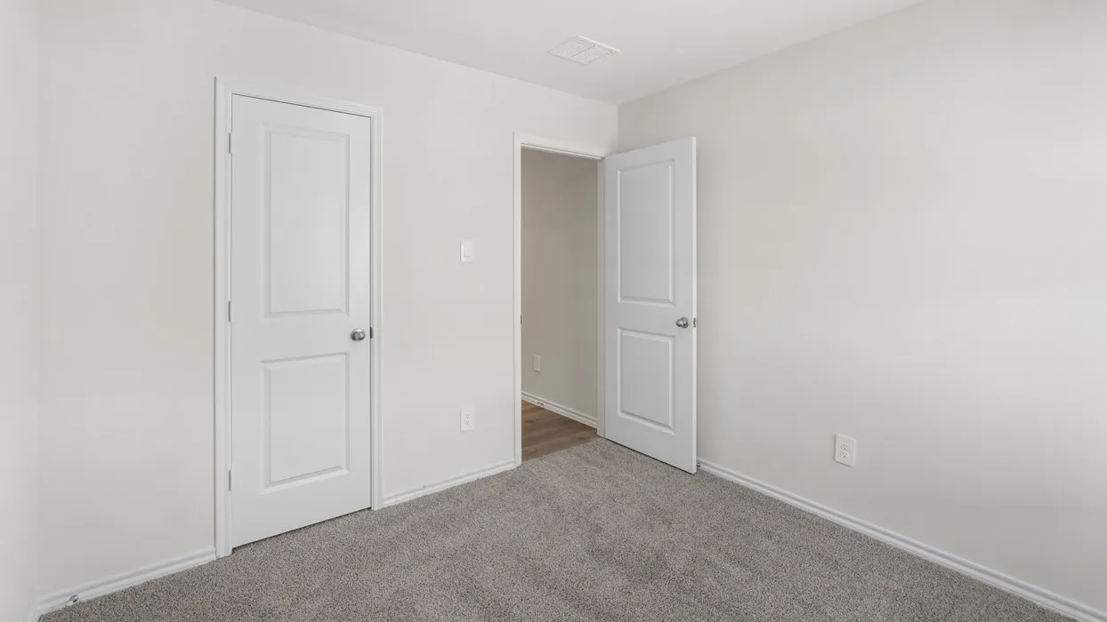 Neutral-toned room featuring a white door with silver hardware, light gray walls, white baseboards, and gray carpet flooring