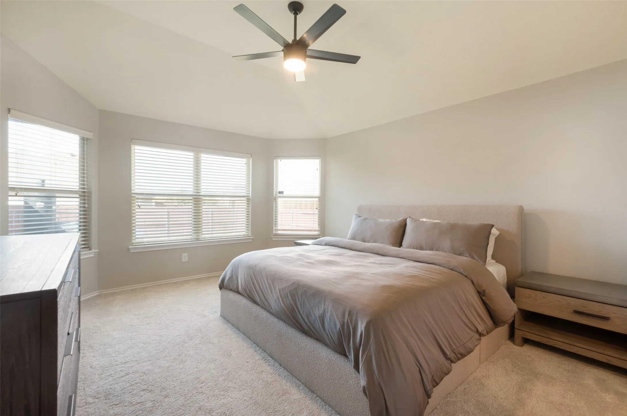 Vaulted ceiling with a flush-mount ceiling fan, multiple windows with blinds, and neutral carpeting