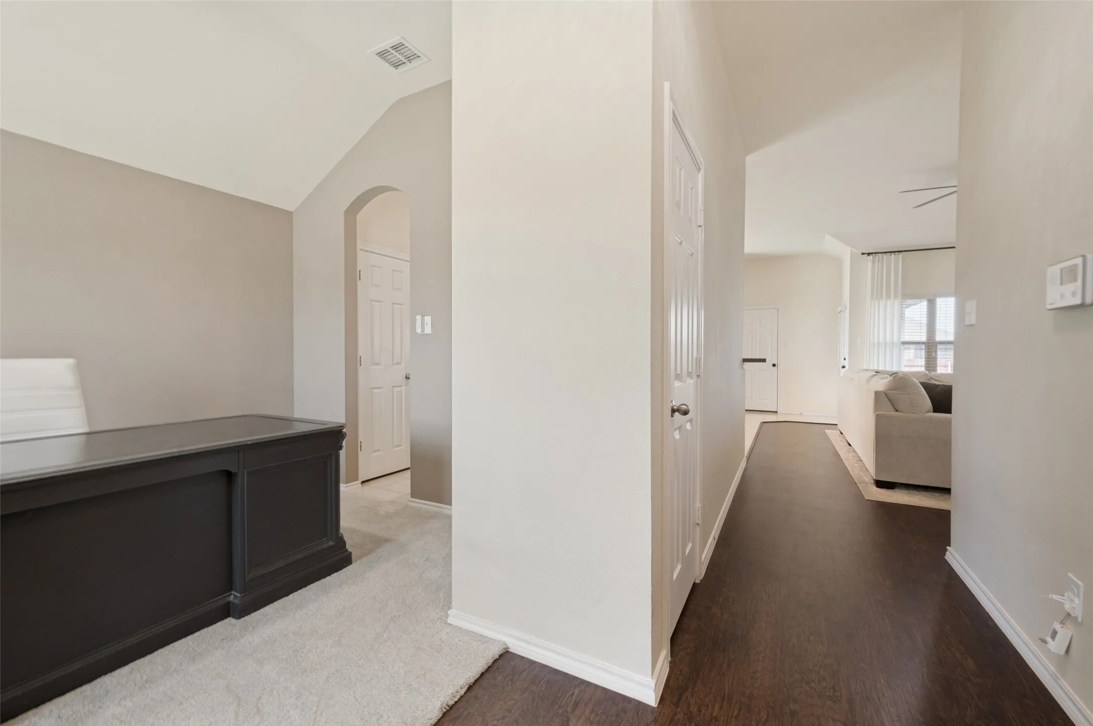 Vaulted ceiling with an arched entryway, dark wood-finish flooring, and light-colored walls