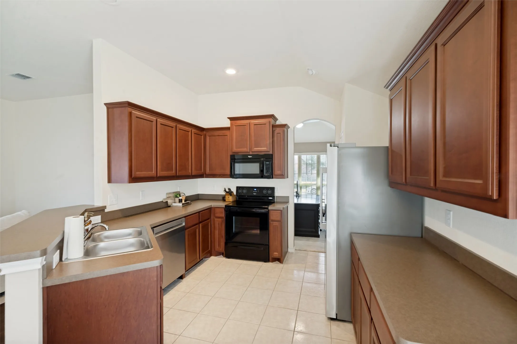 Kitchen featuring wood-finish cabinetry, stainless steel double-basin sink, stainless steel dishwasher, and a full suite of appliances