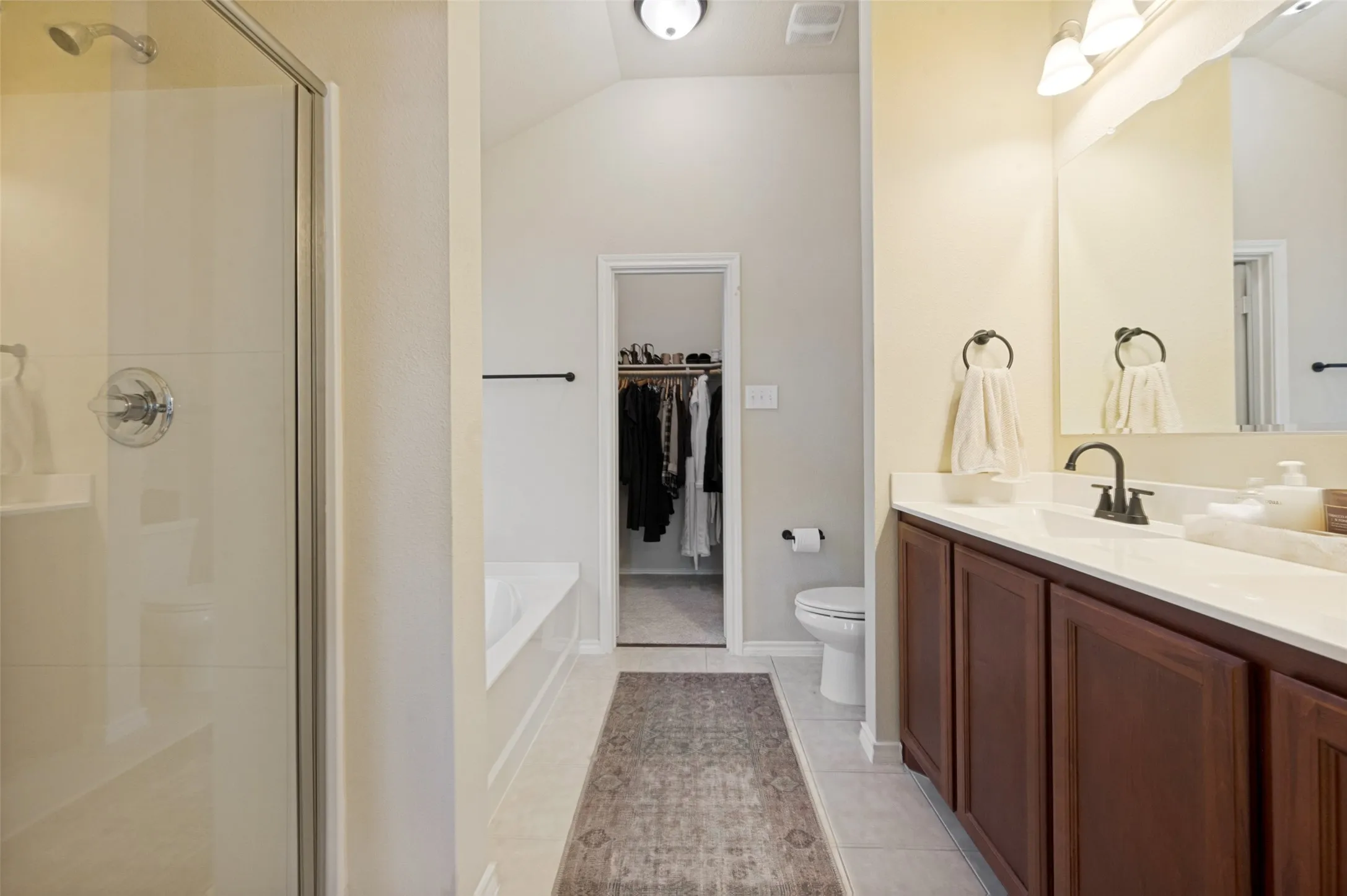 Bathroom featuring a glass-enclosed shower, built-in bathtub, dual-basin vanity with dark wood-finish cabinetry, and a walk-in closet