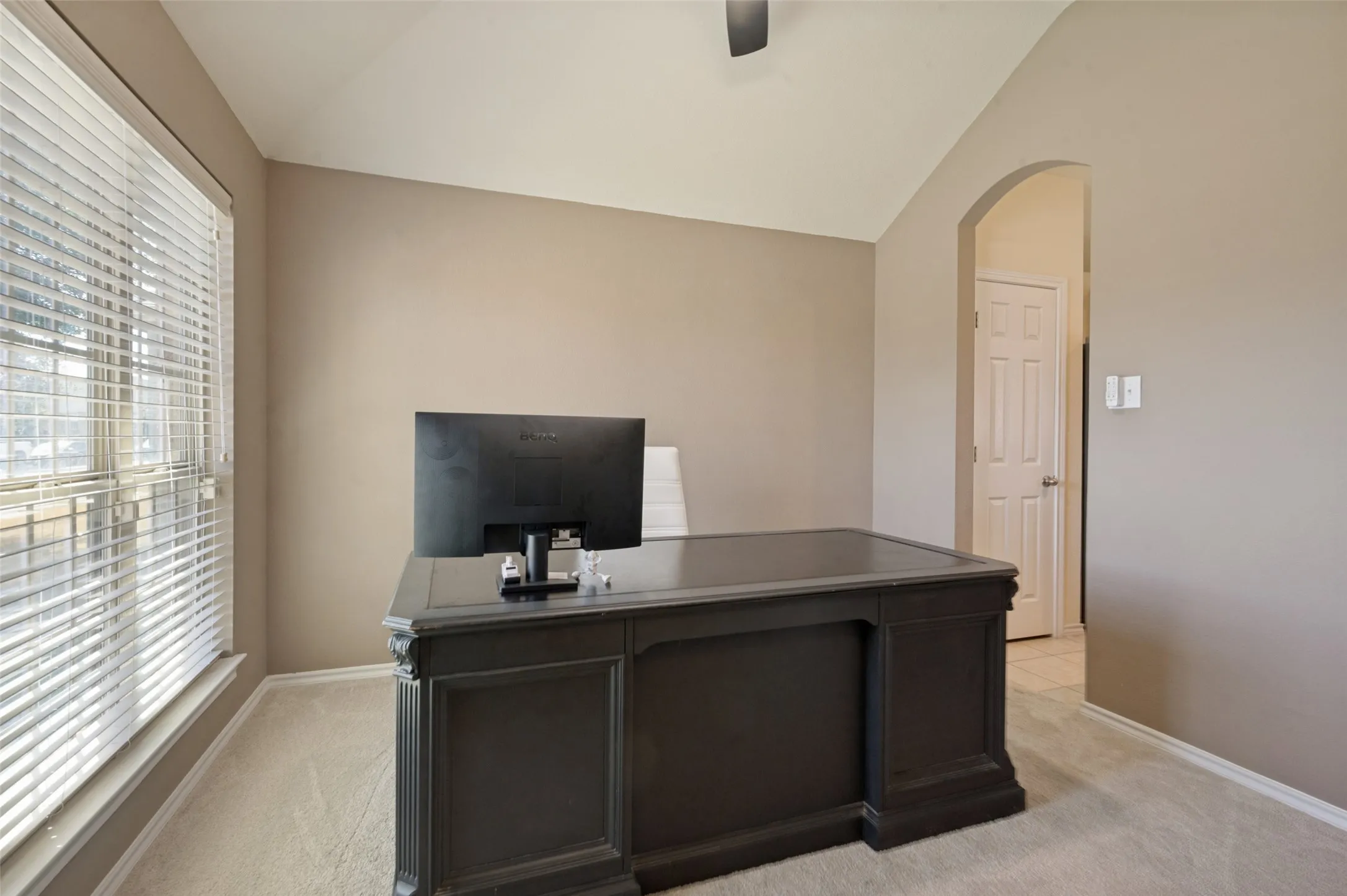 Window with horizontal blinds, neutral wall paint, vaulted ceiling, and an arched doorway