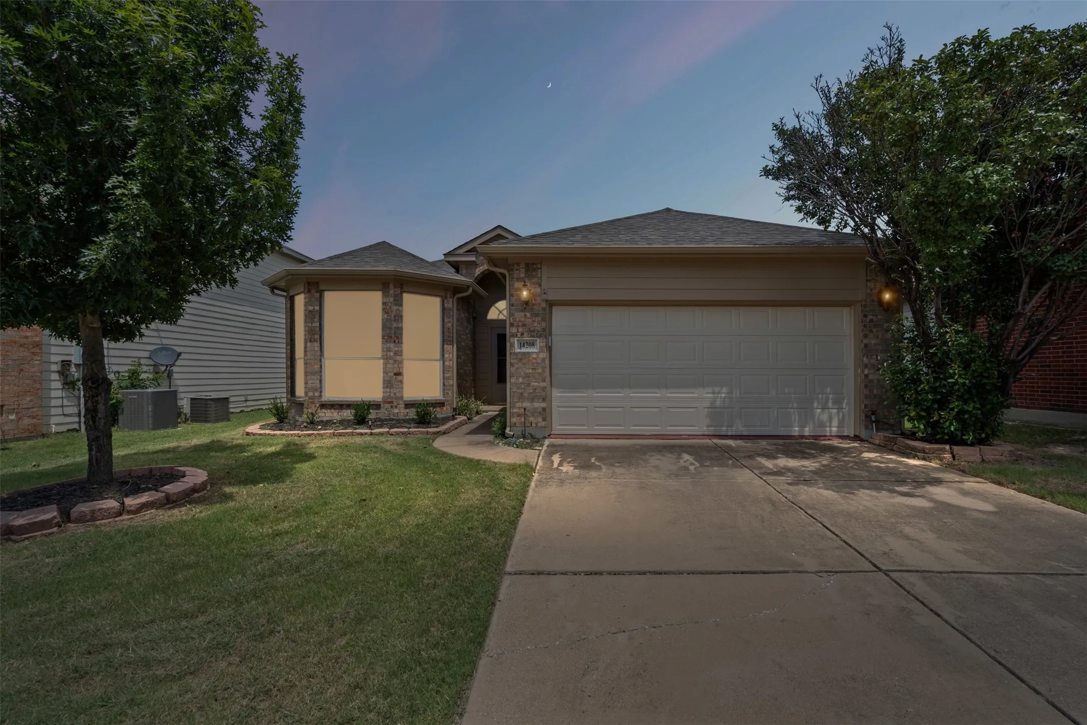 Brick and siding exterior, front yard with mature trees, established landscaping, and a concrete driveway