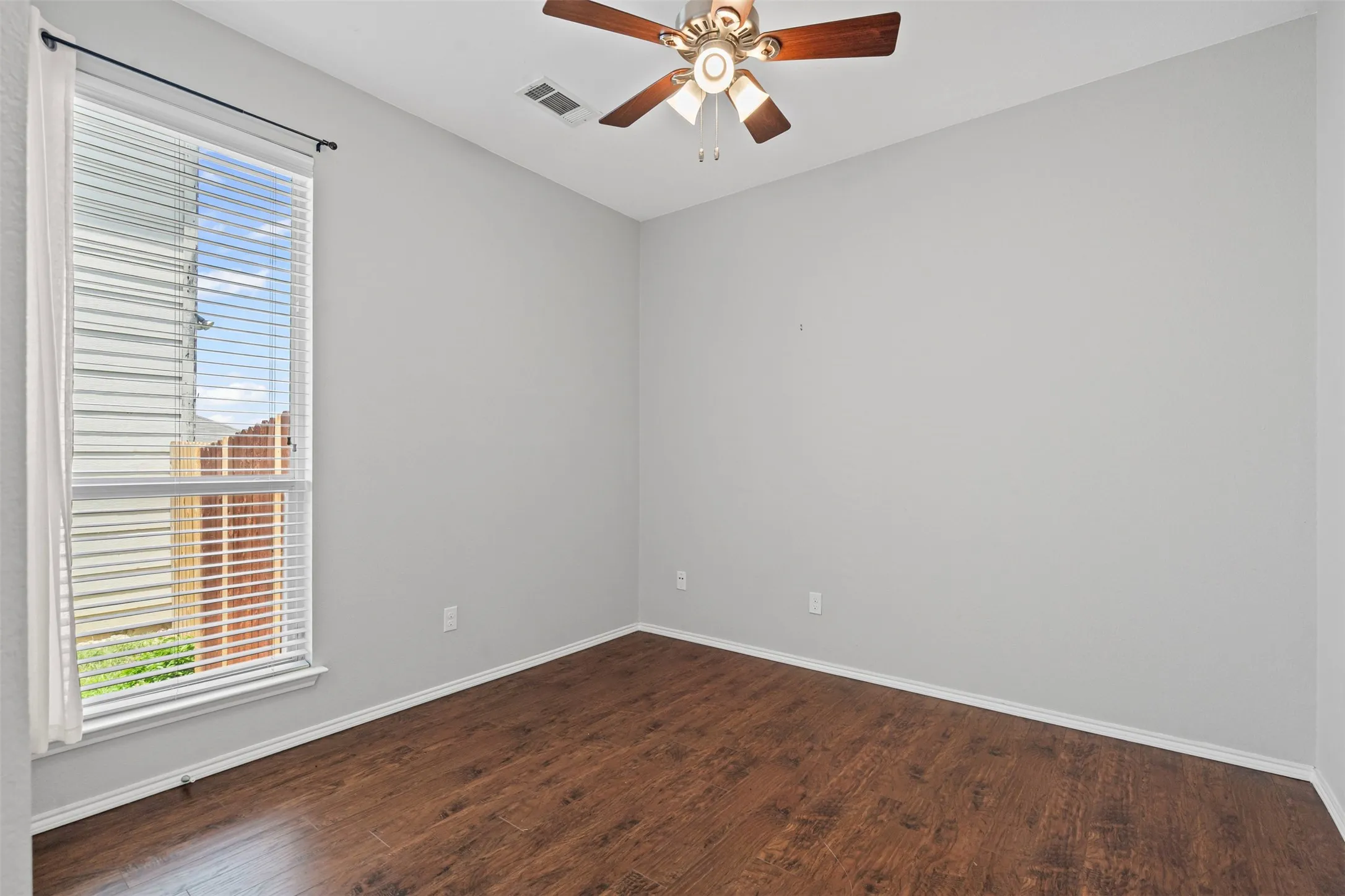 Wood-finish flooring with light gray walls, a ceiling fan with light fixture, and a large window with blinds