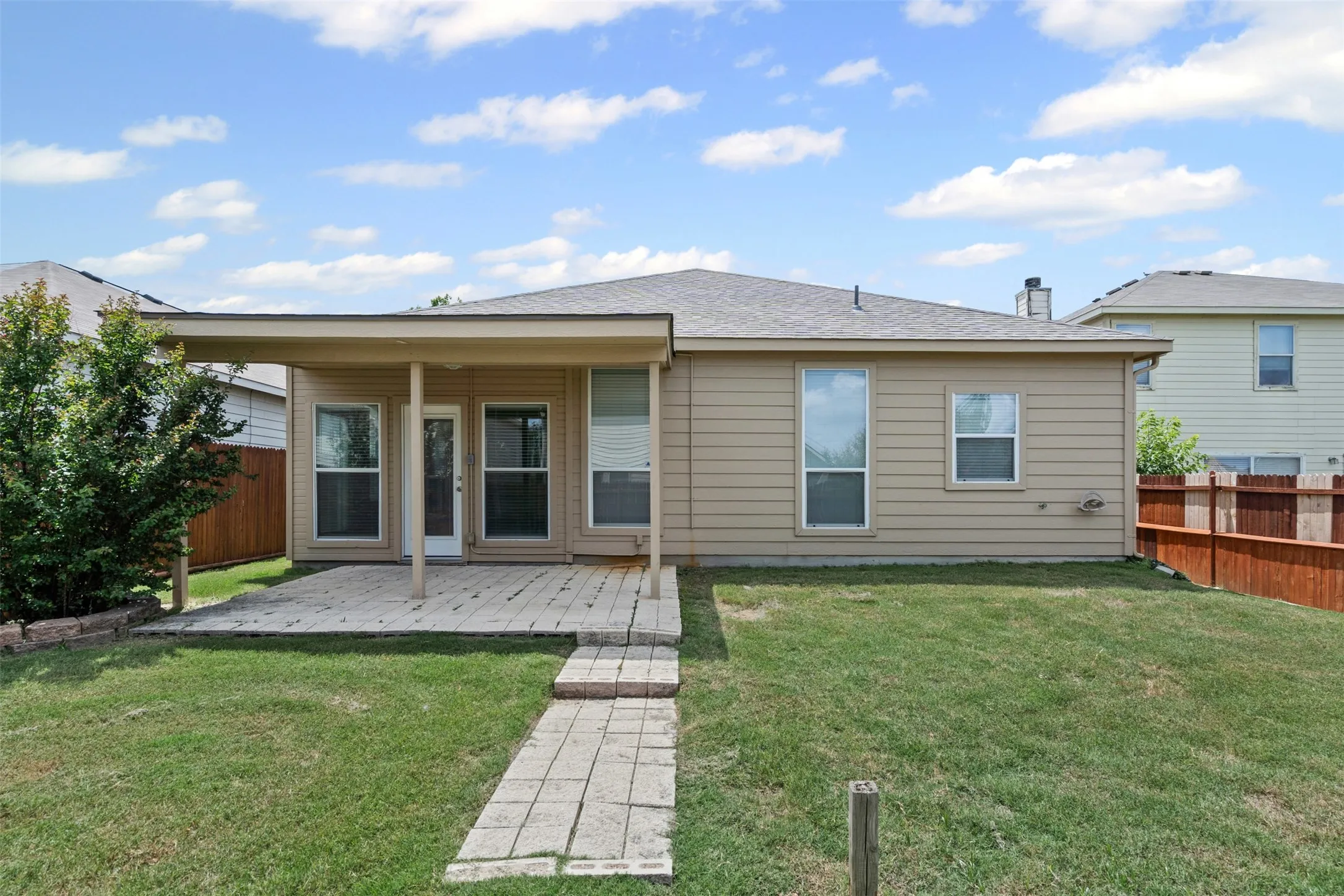 Expansive backyard featuring a covered patio, paved walkway, and a privacy fence