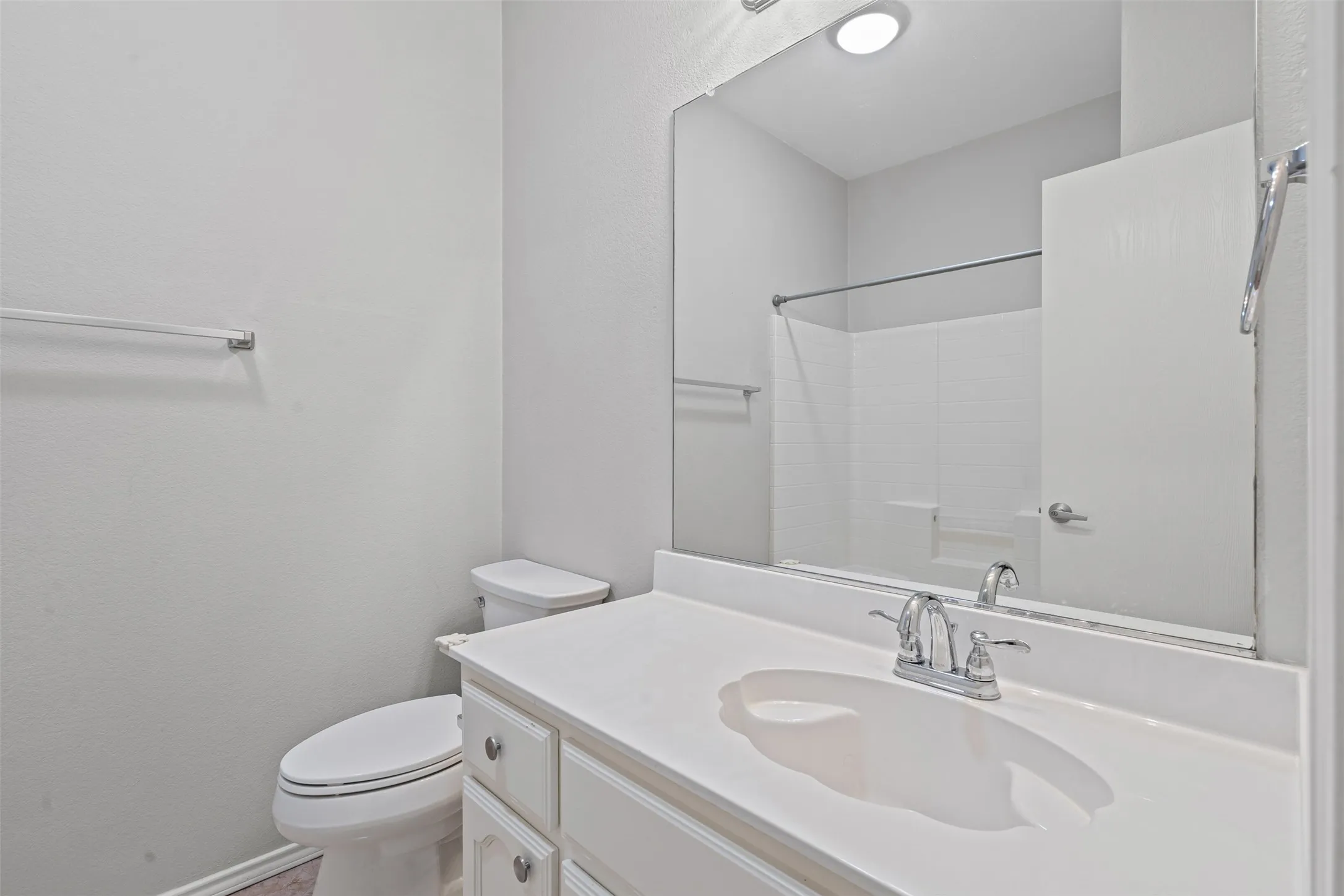 Integrated sink and countertop, white cabinetry with silver hardware, full vanity mirror, and a shower with a white tiled surround