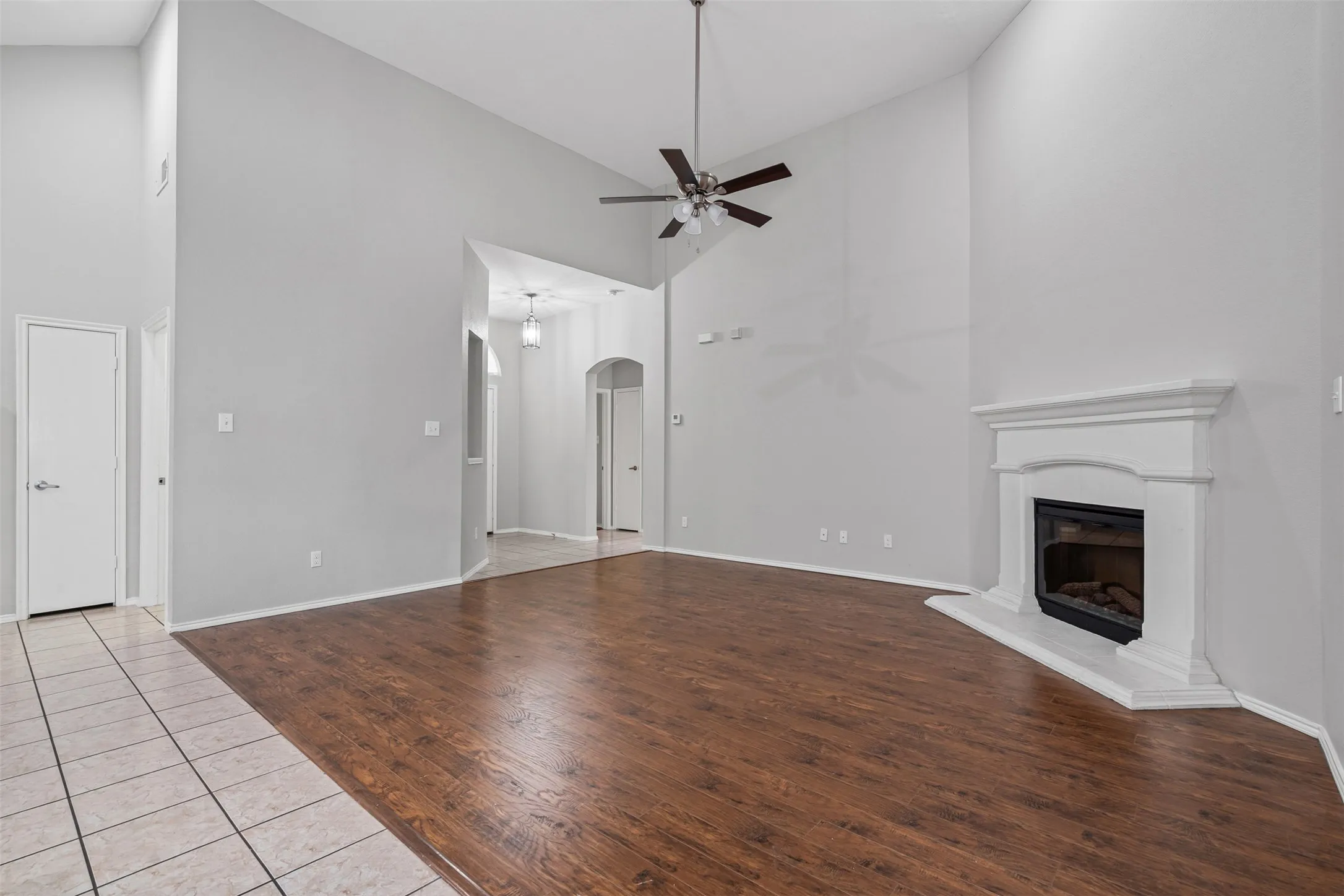 Vaulted ceiling with a ceiling fan, fireplace with a white mantel, wood-finish flooring, and arched entryway