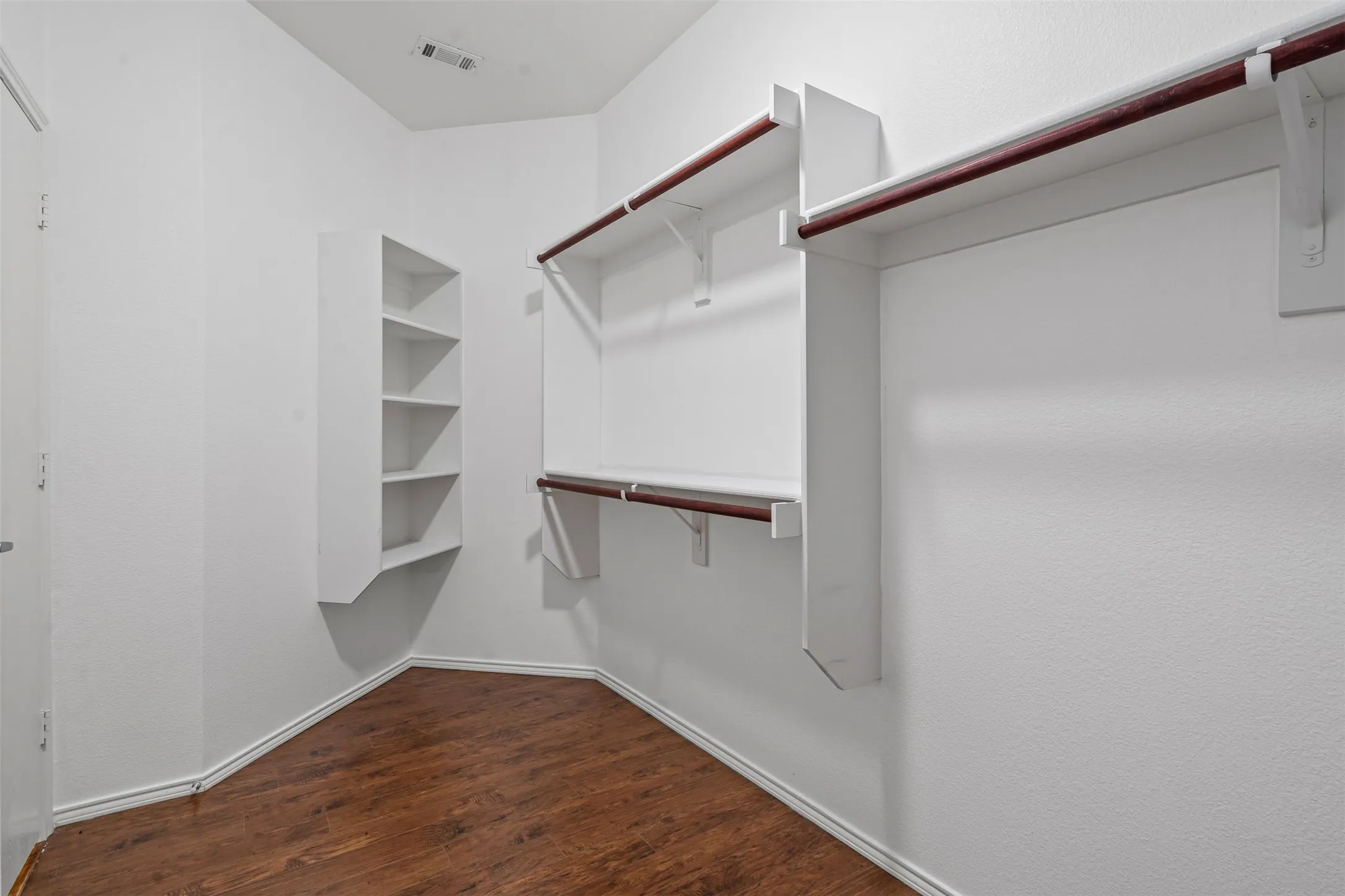 Walk-in closet featuring wood-finish flooring, built-in shelving, and multiple hanging rods
