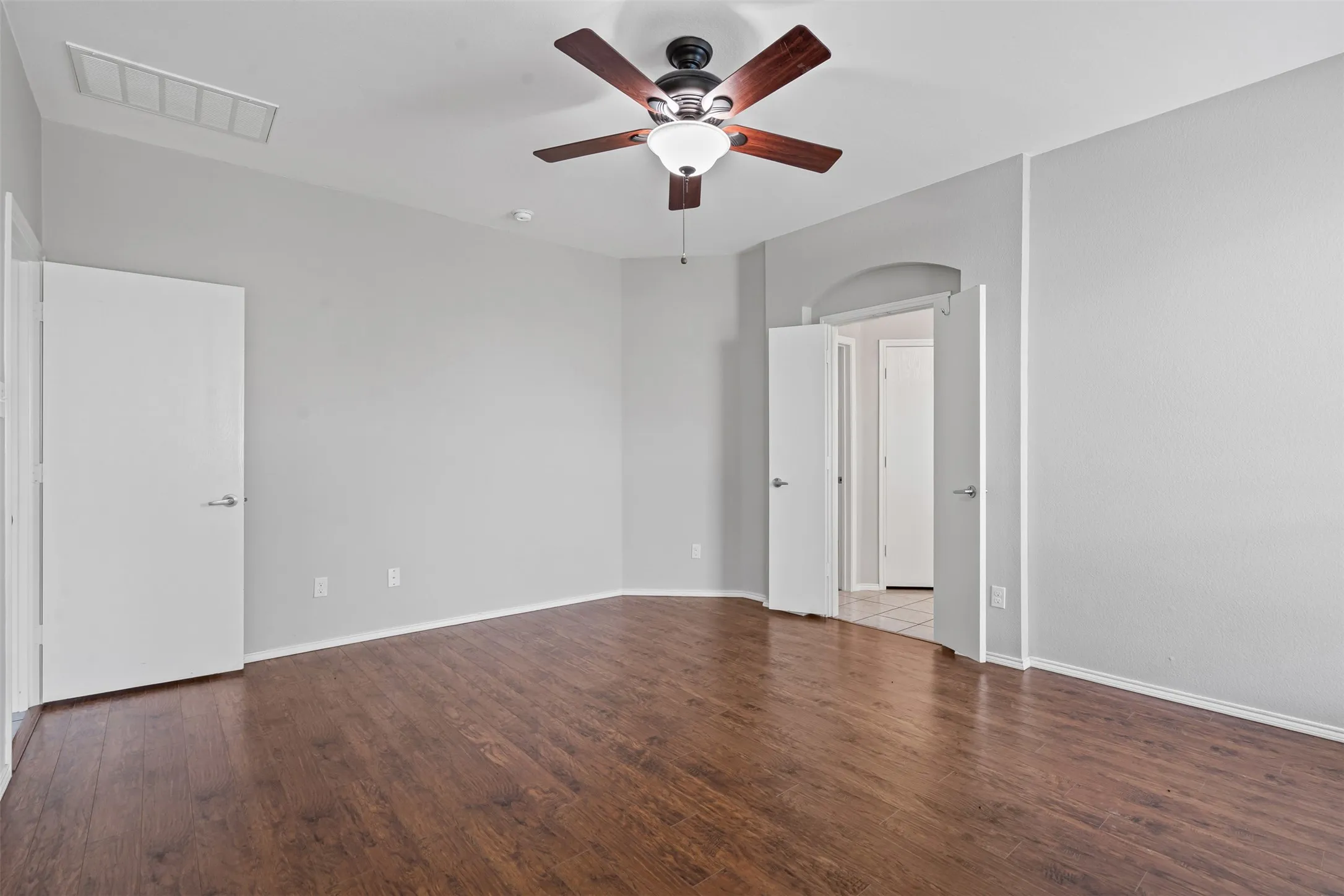 Wood-finish flooring, ceiling fan with integrated lighting, arched doorway, and neutral wall tones
