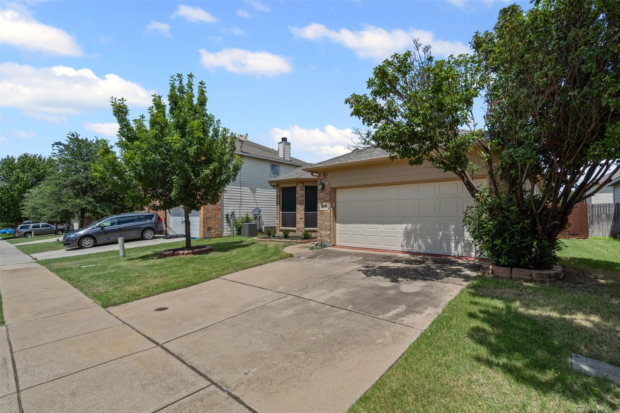 Attached two-car garage with a sectional door, concrete driveway, stone facade accents, and manicured landscaping