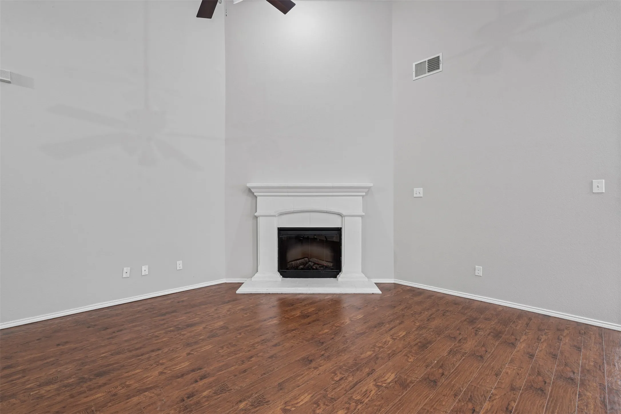Voluminous ceiling height, wood-finish flooring, decorative fireplace, ceiling fan, and light gray wall paint