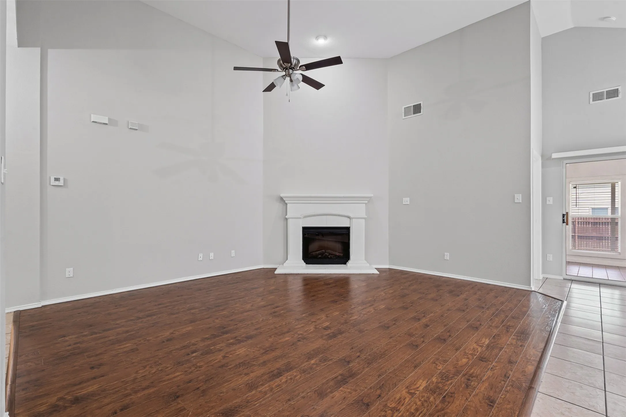 Vaulted ceiling, wood-finish flooring, ceiling fan, fireplace with white mantel, and sliding glass door