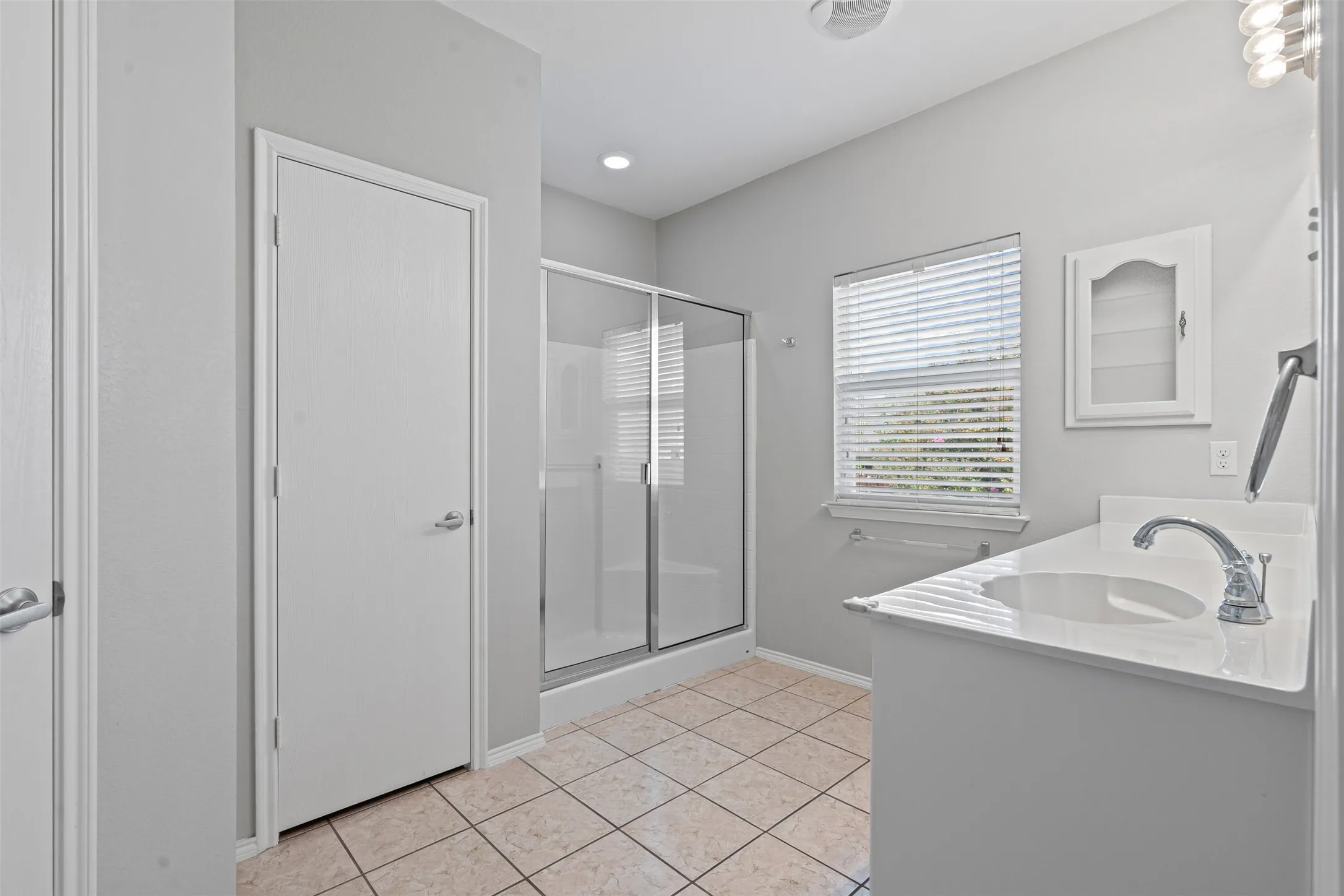 Tiled flooring, single vanity with integrated sink, shower with glass enclosure, recessed lighting, and a window with blinds