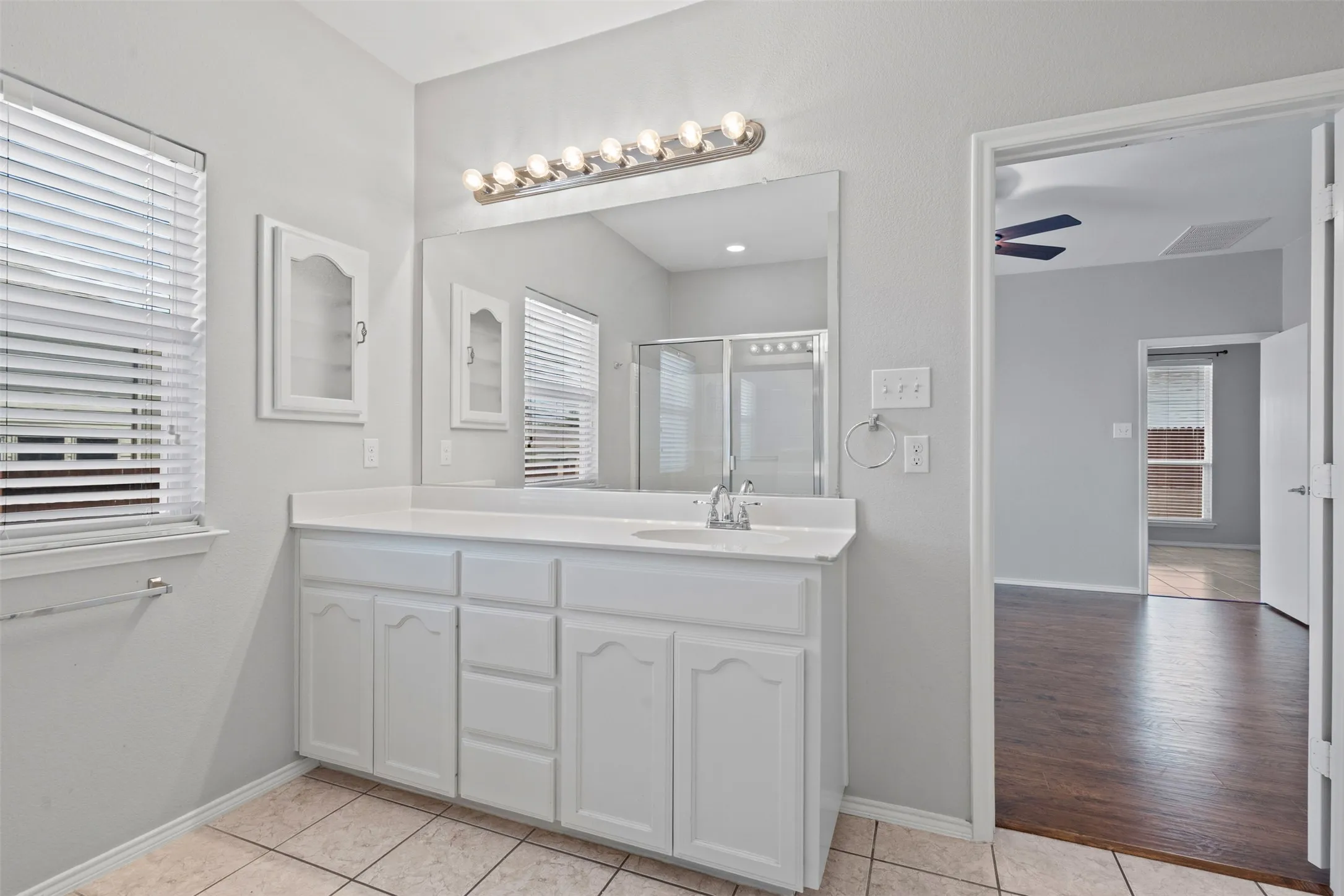 Dual sink vanity with white cabinetry, integrated mirror, and a shower enclosure with sliding glass doors