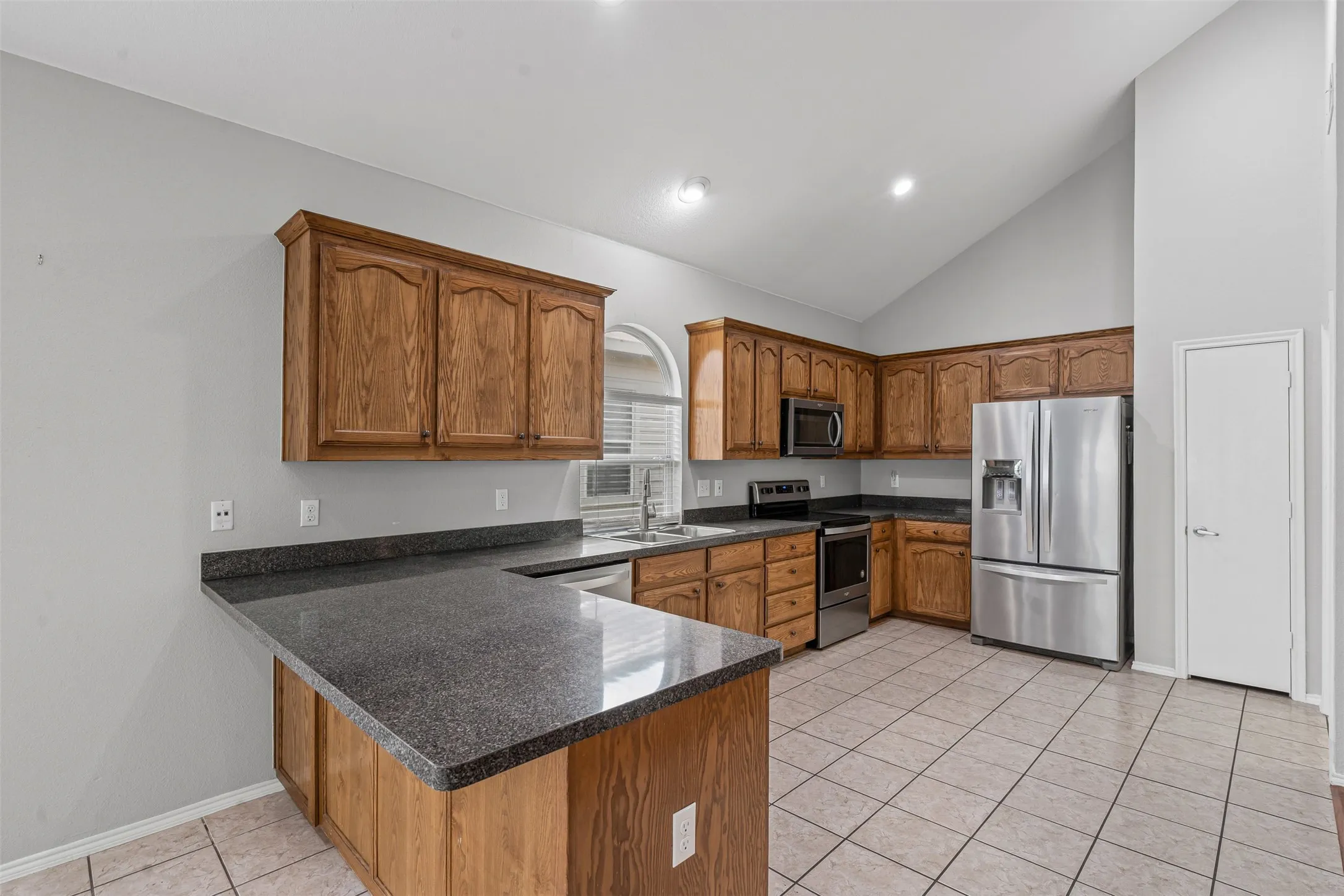 Kitchen featuring wood cabinetry, dark countertops, stainless steel appliances, and a vaulted ceiling