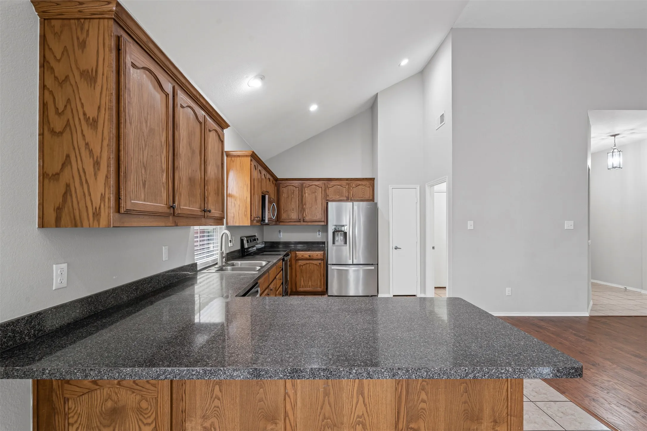 Kitchen featuring wood cabinetry, dark stone countertops, stainless steel appliances, recessed lighting, and a vaulted ceiling