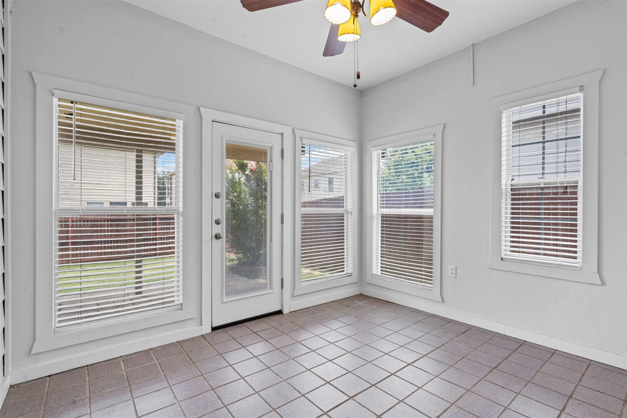 Tiled flooring, multiple windows with blinds, a glass-paneled door, and a ceiling fan with integrated lighting