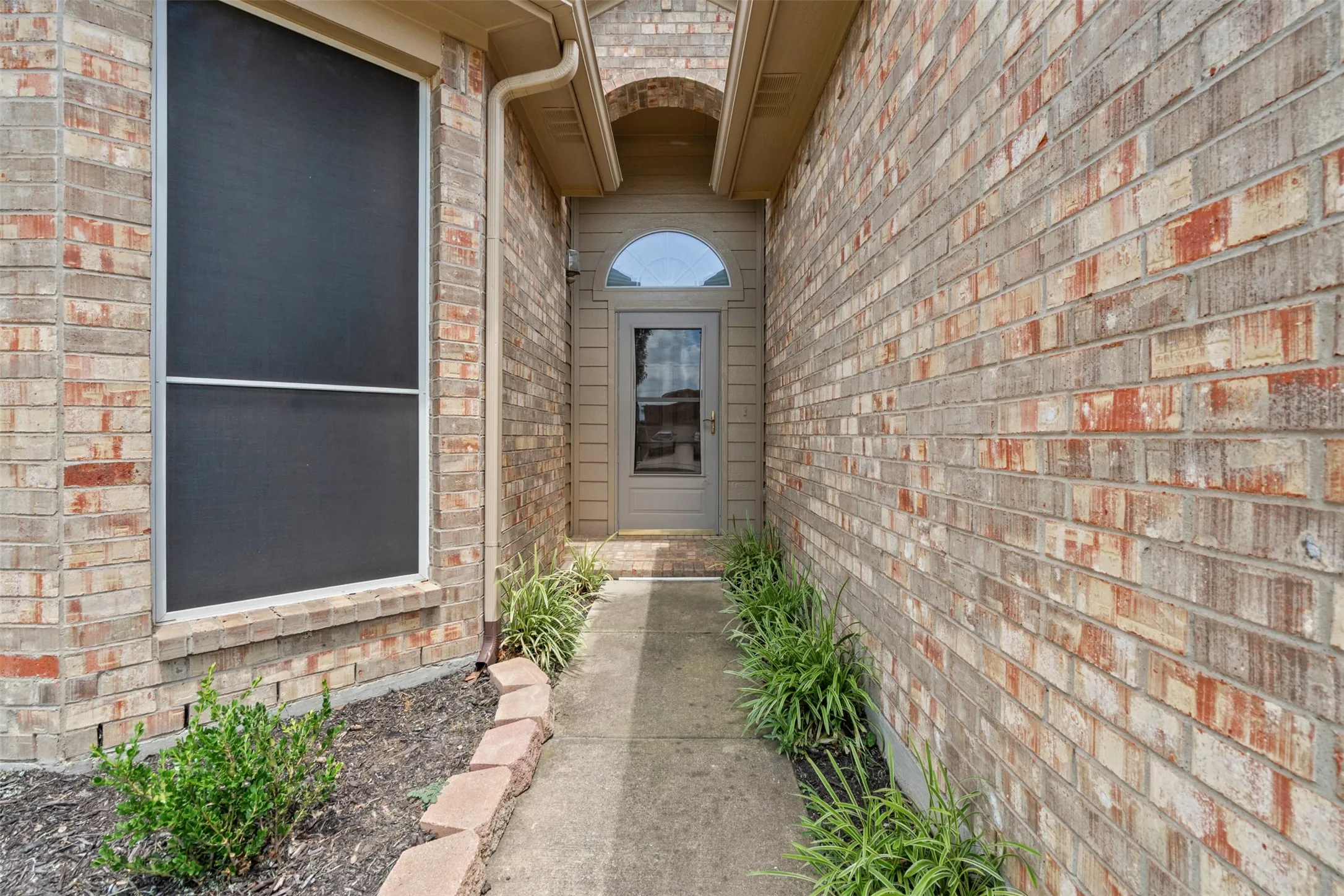 Brick exterior with a covered entry, concrete walkway, and landscaped planting beds