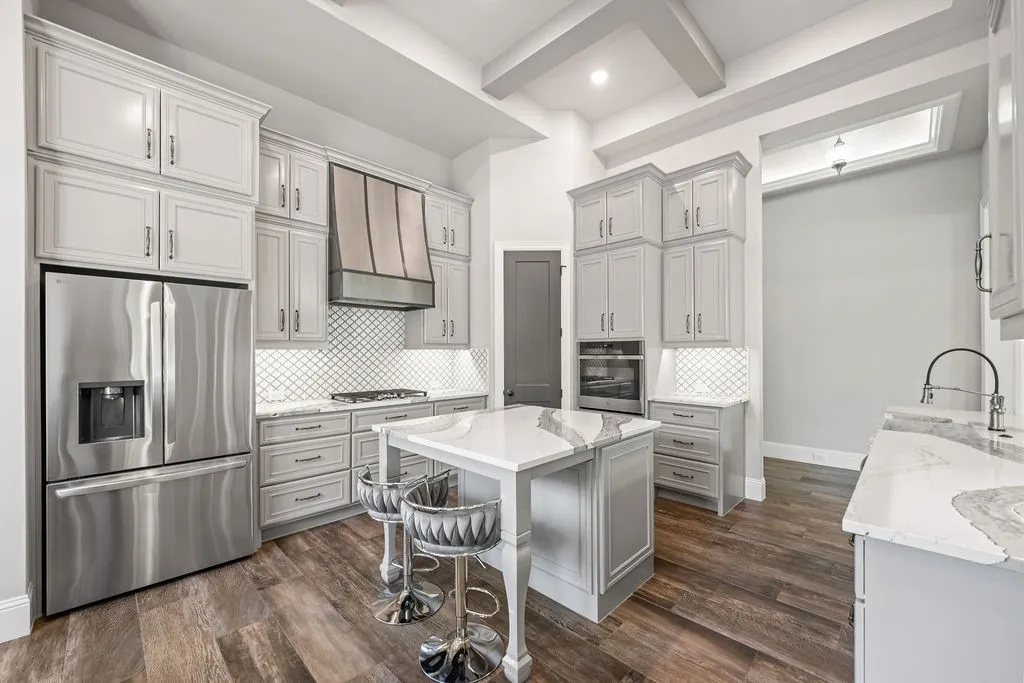 White shaker cabinetry with crown molding, stainless steel appliances, patterned tile backsplash, wood-finish flooring, and a kitchen island with stone countertop