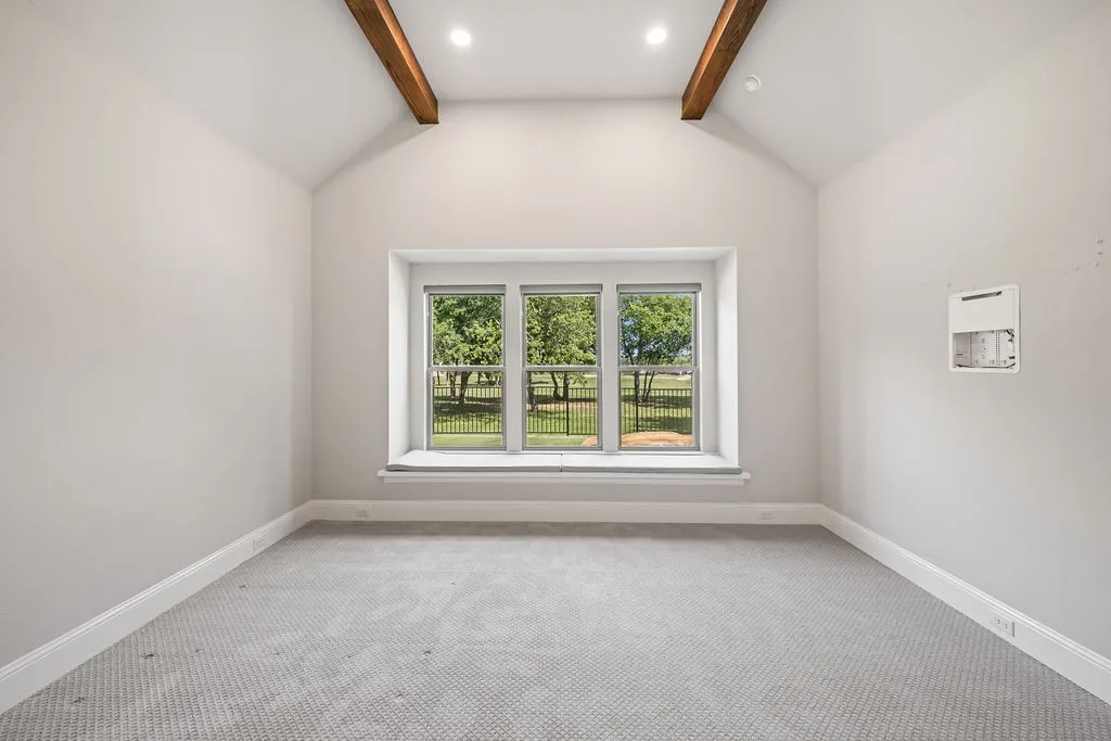 Vaulted ceiling with exposed wood beams, recessed lighting, triple window with deep sill, and light gray patterned carpeting