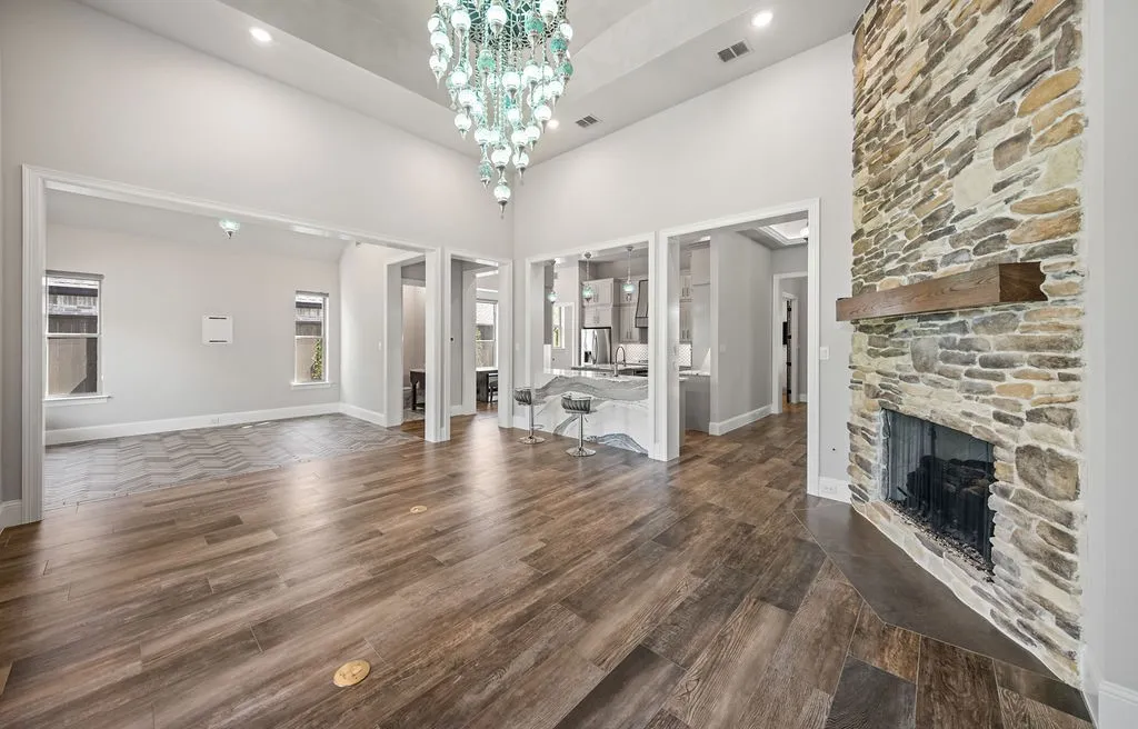 Vaulted ceilings with recessed lighting, wood-finish flooring, full-height stone fireplace with wood mantel, and a multi-tiered chandelier