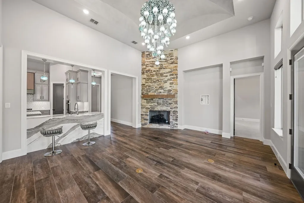 Expansive open-concept living area featuring high vaulted ceilings, wood-finish flooring, a stone-clad fireplace with a wood mantle, and a kitchen pass-through with a waterfall-edge countertop