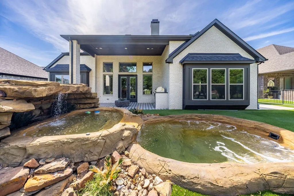 Exterior featuring white brick, dark trim, a covered patio, and a multi-level rock water feature