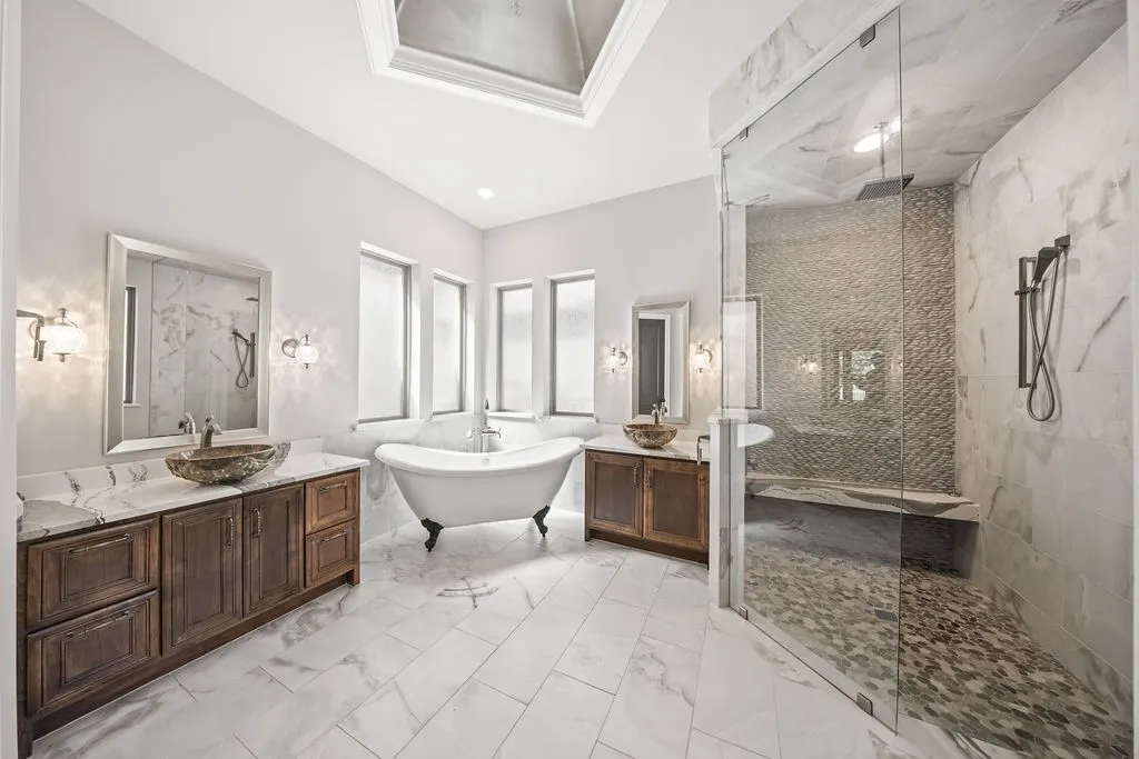 Freestanding clawfoot tub, dual wood-finish vanities with vessel sinks, walk-in shower with bench seating, and skylight