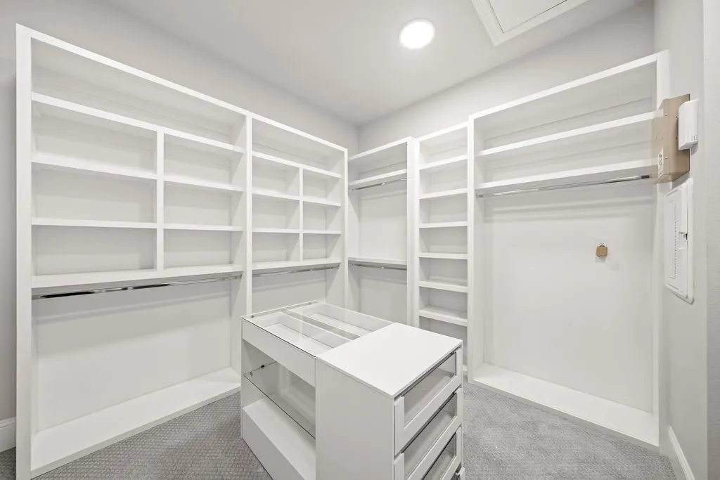 Built-in custom shelving, central island with glass top, multiple hanging rods, recessed ceiling lighting, and carpet flooring