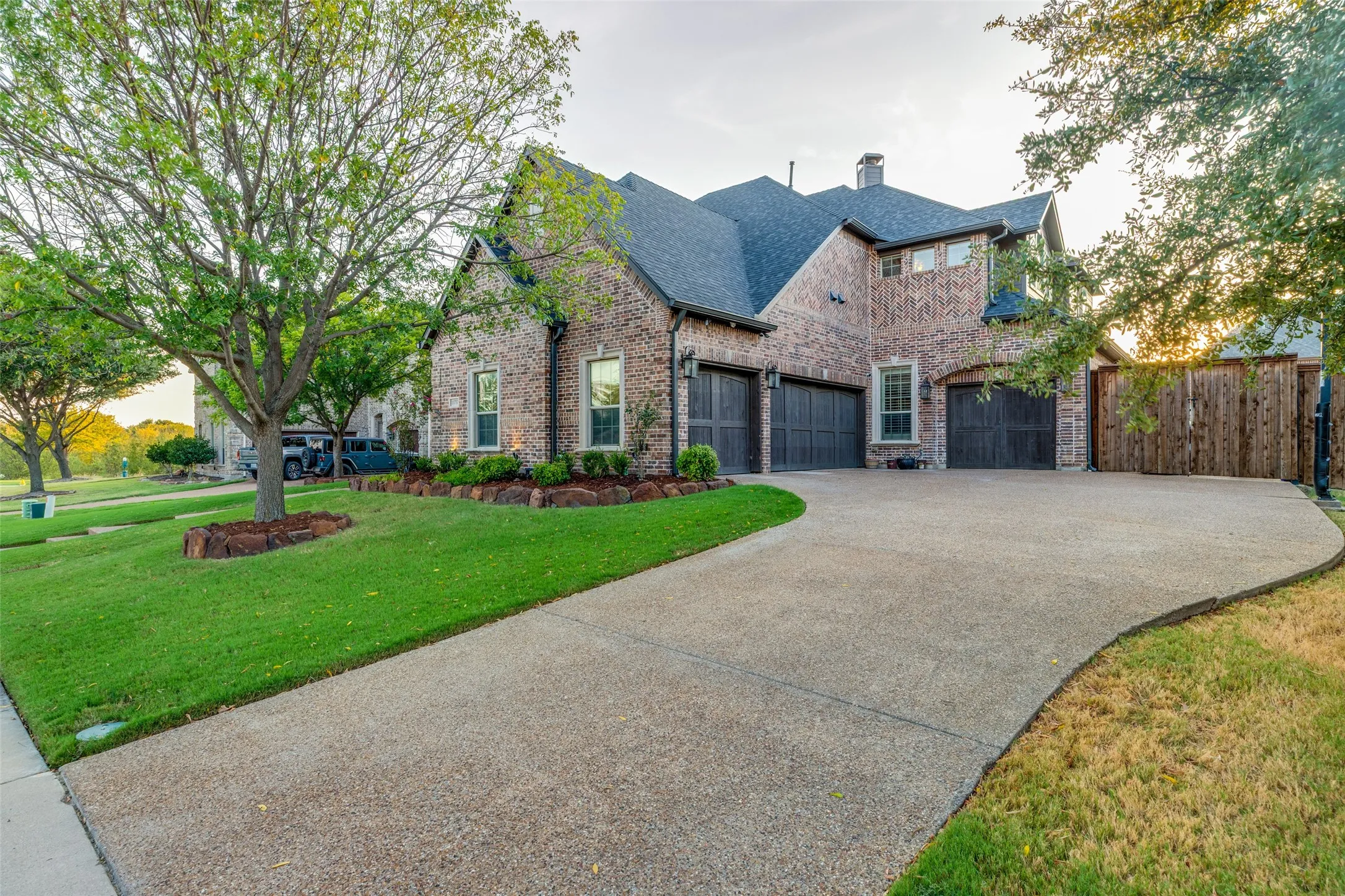 Brick exterior construction, four car garage with arched entries, asphalt shingle roof, well-maintained lawn, and mature trees