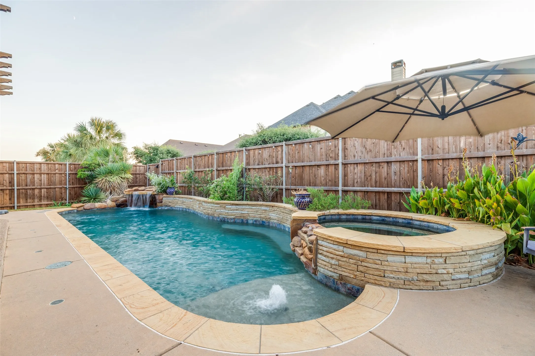 Swimming pool with an integrated spa, stone-clad waterfall feature, and surrounding concrete decking