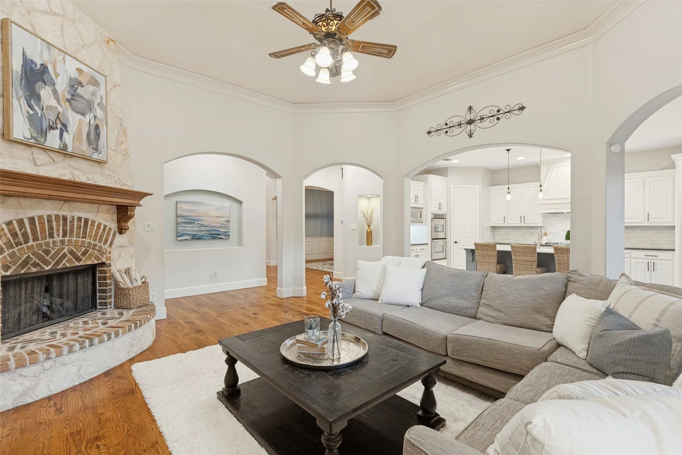 Vaulted ceiling with crown molding, wood-finish flooring, stone-clad fireplace with brick hearth, multi-pane windows, and beautiful Newcastle Arches