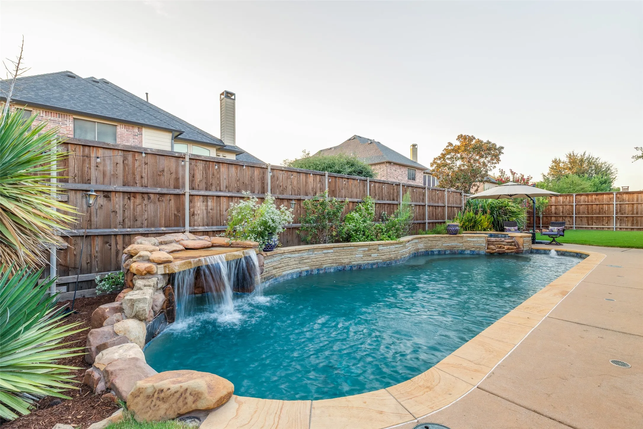 Freeform pool with a stone waterfall feature, integrated spa, and concrete decking