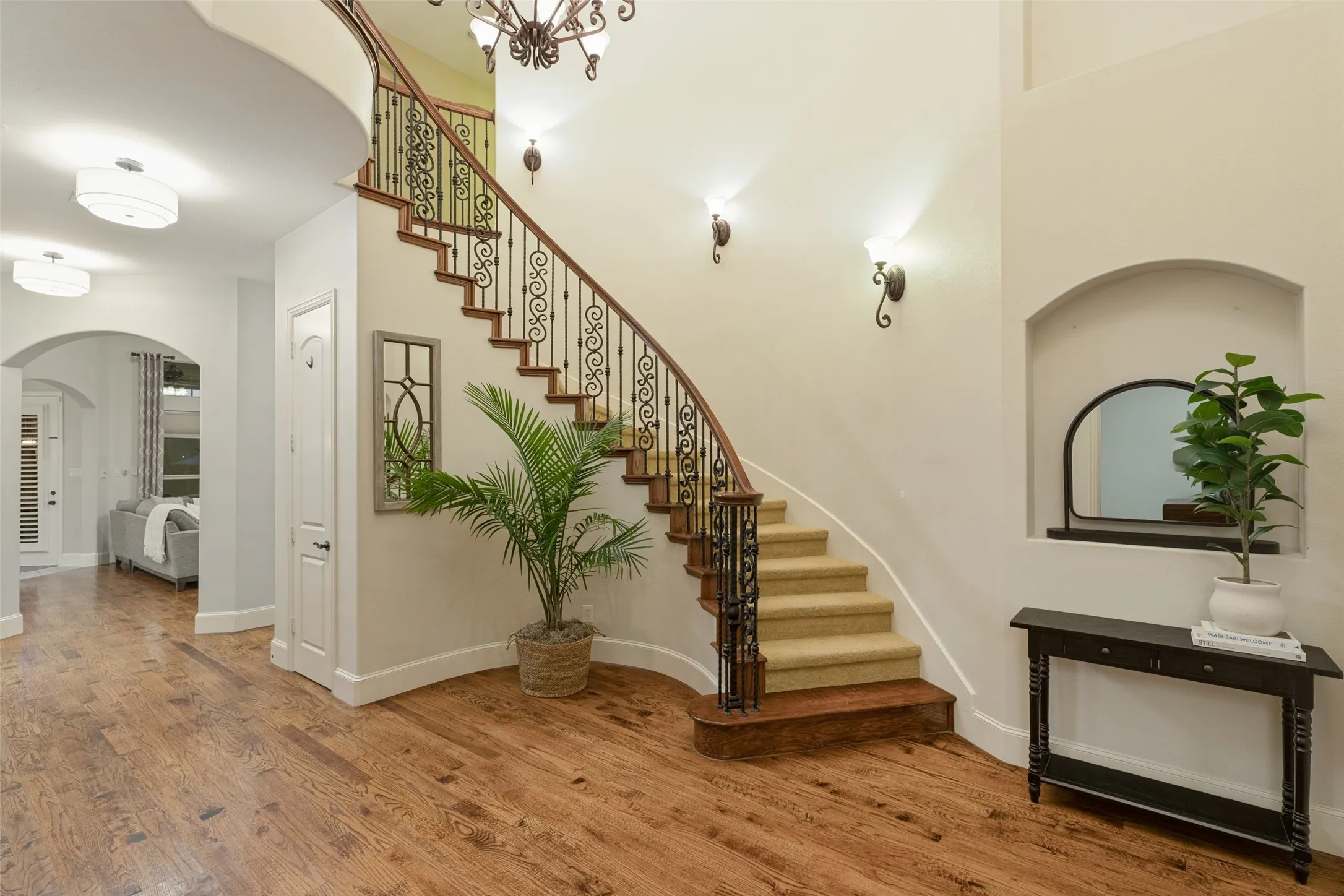 Curved staircase with wrought iron balusters, wood-finish flooring, recessed wall niche, and arched doorways