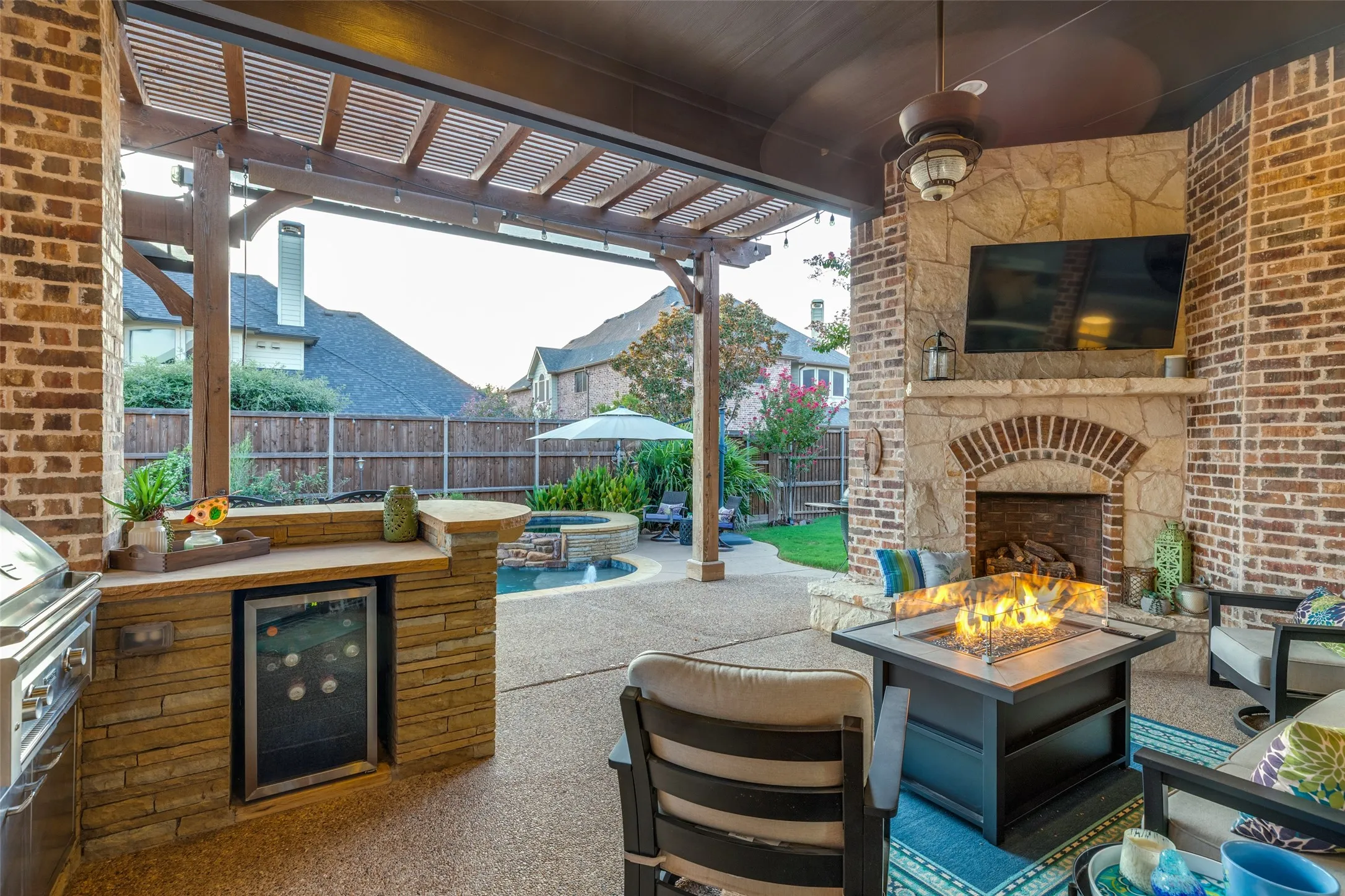 Covered outdoor living space featuring a stone fireplace, built-in outdoor kitchen with beverage cooler, grill, and prep space