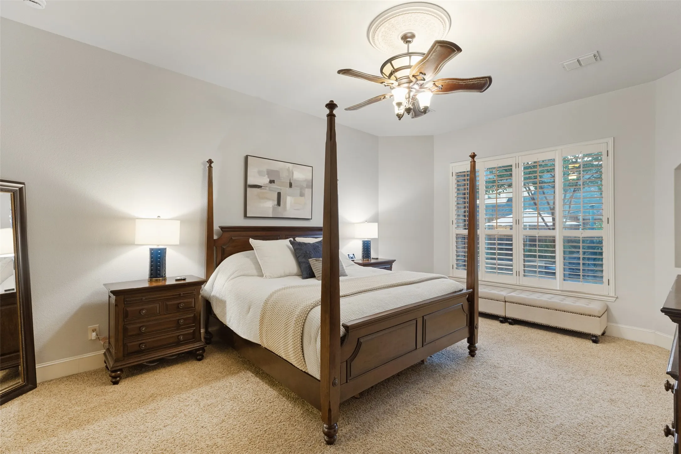 Primary Bedroom with Carpet, ceiling fan with light fixture, windows that face backyard oasis with plantation shutters.