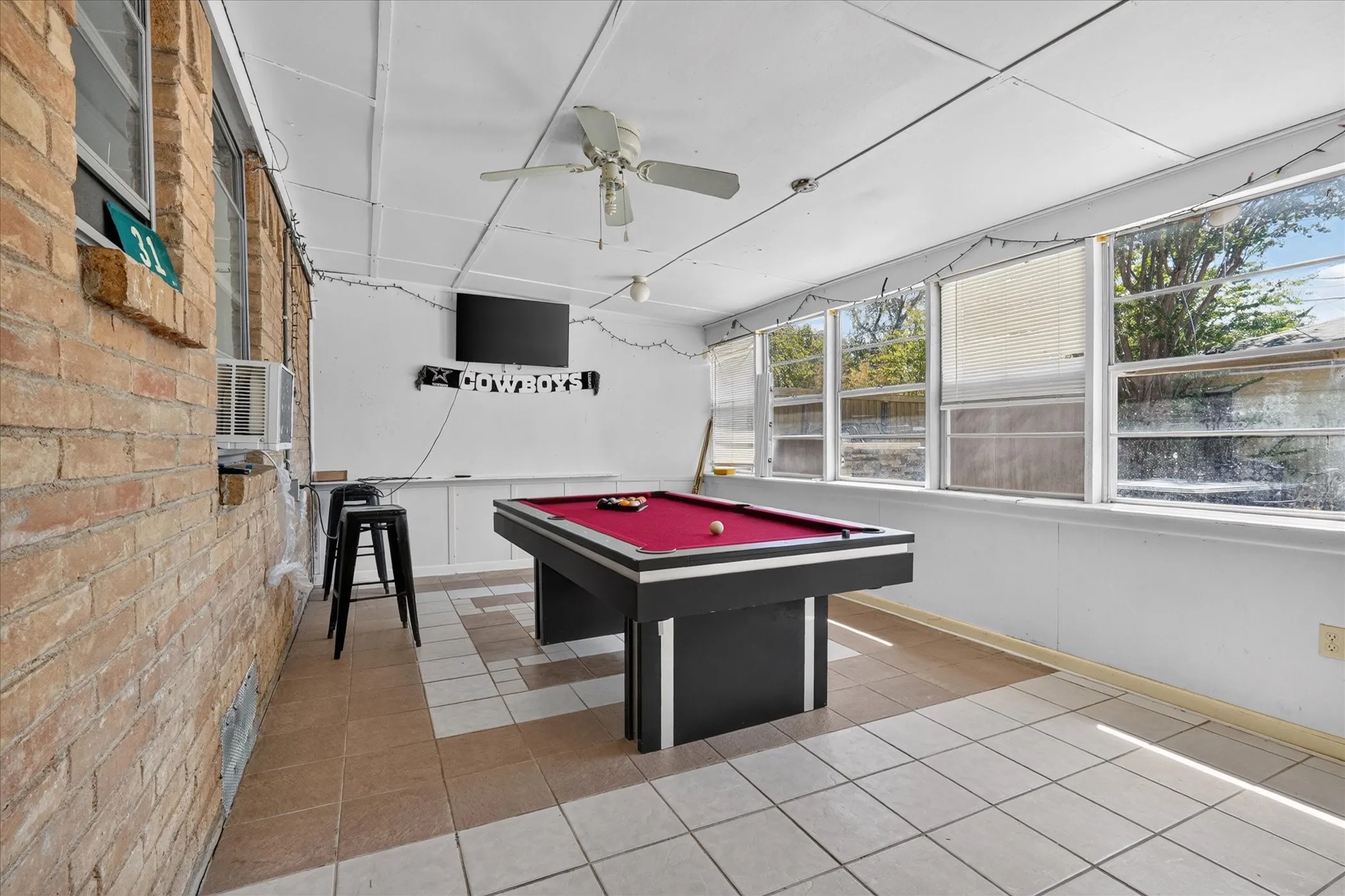 Enclosed patio space featuring brick wall, ceiling fan, and tiled flooring