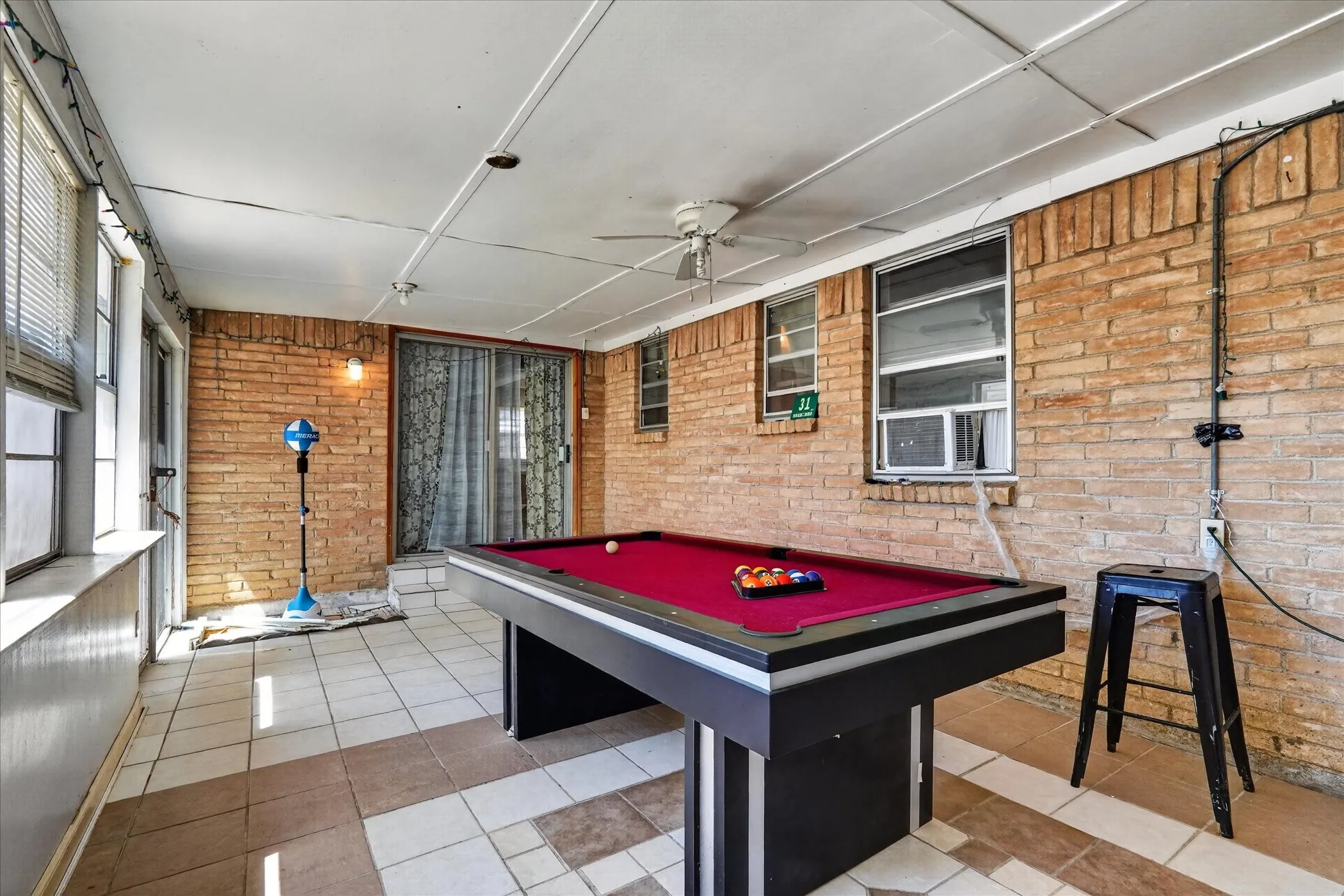 Enclosed patio featuring brick walls, a tile floor, multiple windows, a ceiling fan, and a sliding glass door