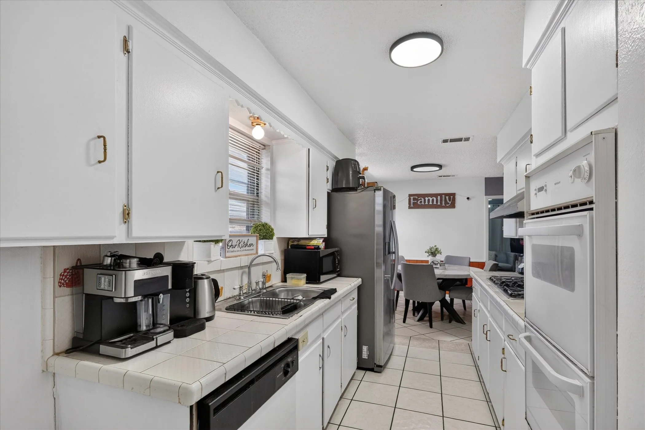 Galley kitchen featuring white cabinetry, tile countertops, stainless steel refrigerator, and built-in oven