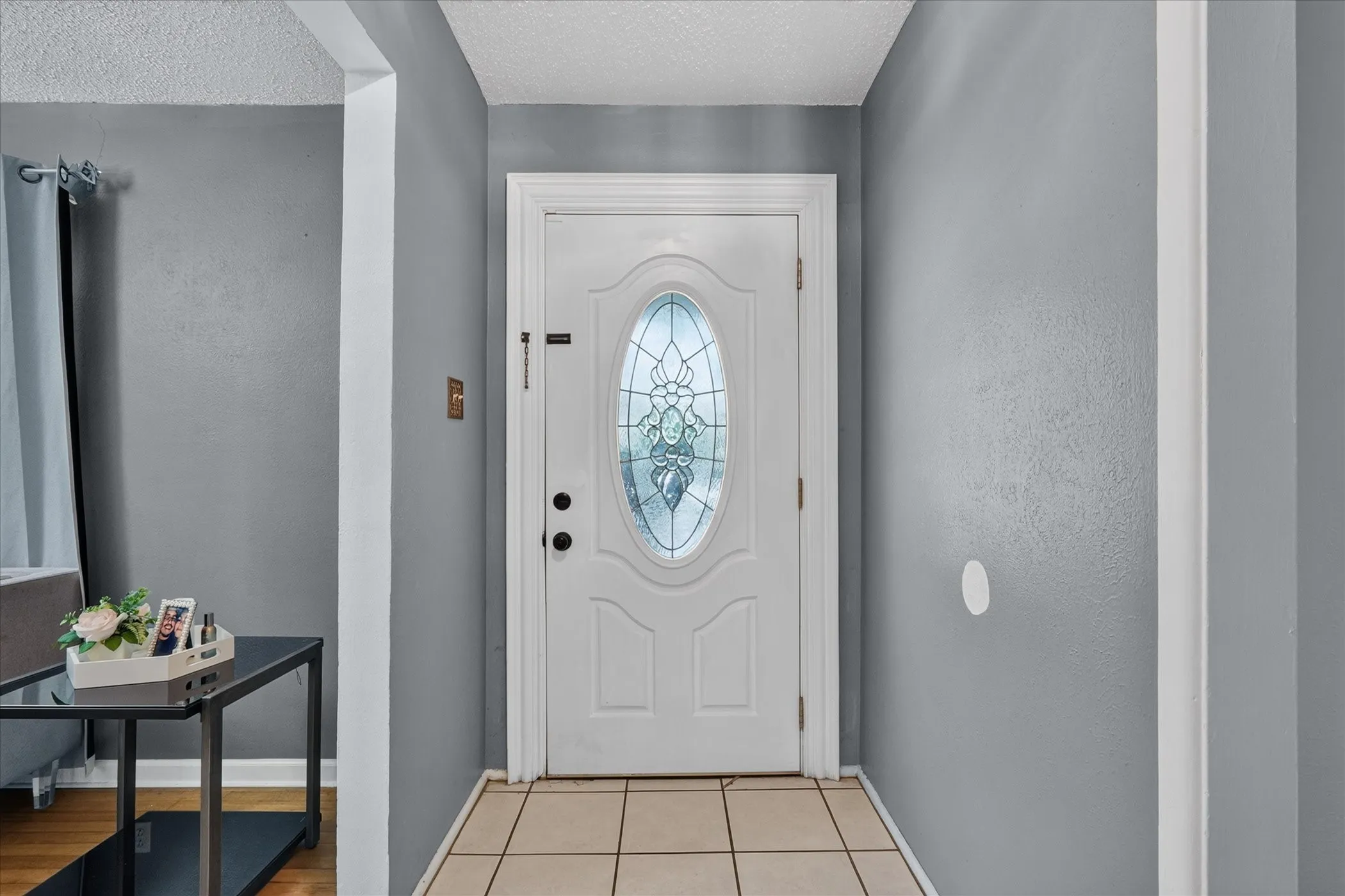 Entryway featuring a white paneled door with an oval stained-glass insert and square tile flooring