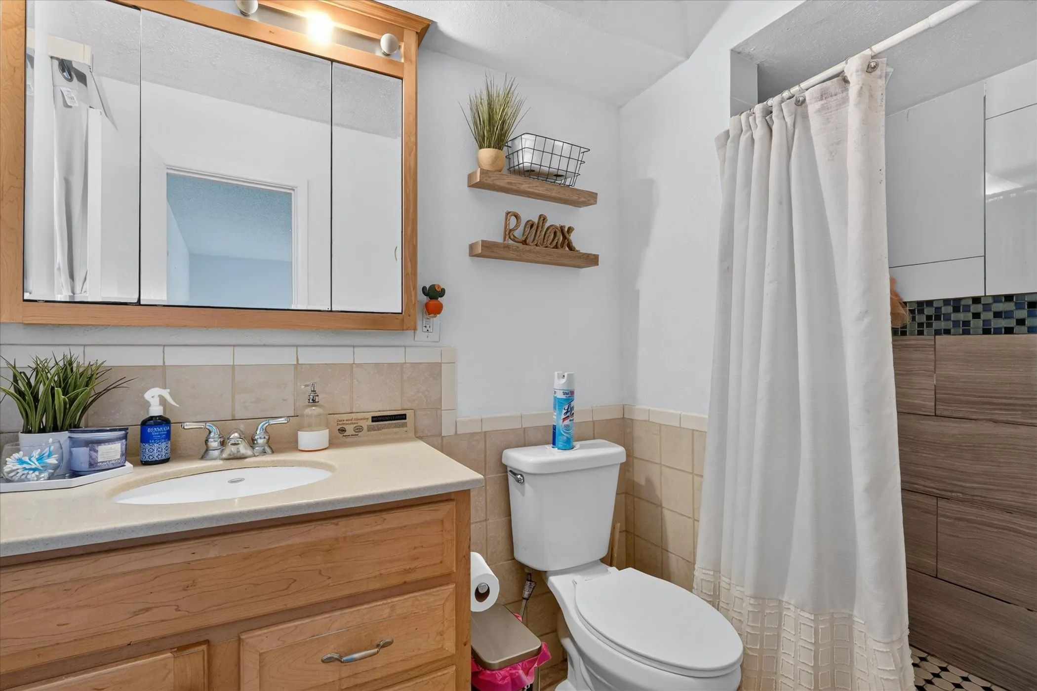 Wood vanity with a built-in sink, medicine cabinet with integrated lighting, and mosaic tile shower surround