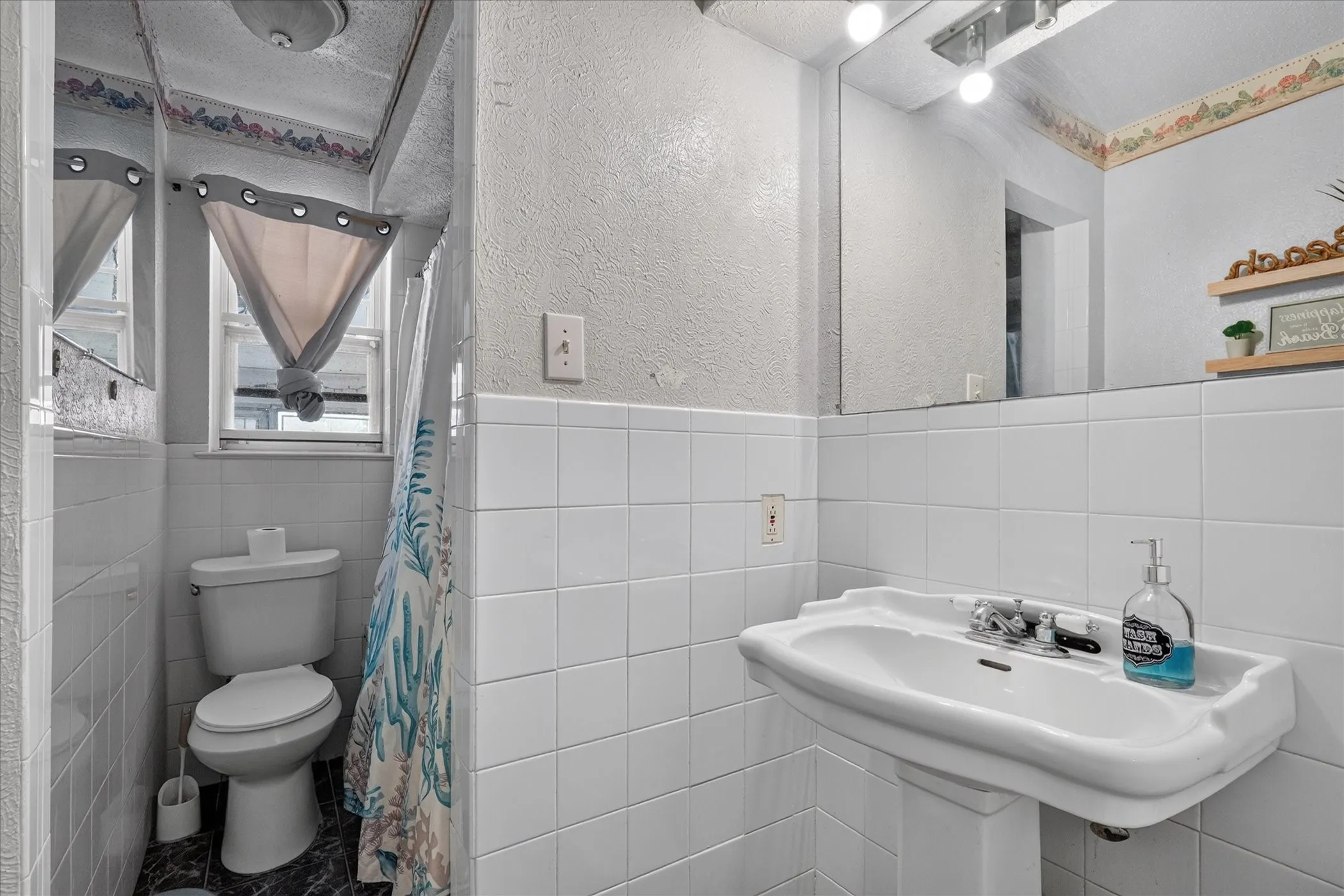 White pedestal sink with chrome-finish fixtures, a wall-mounted mirror, and white tiled walls