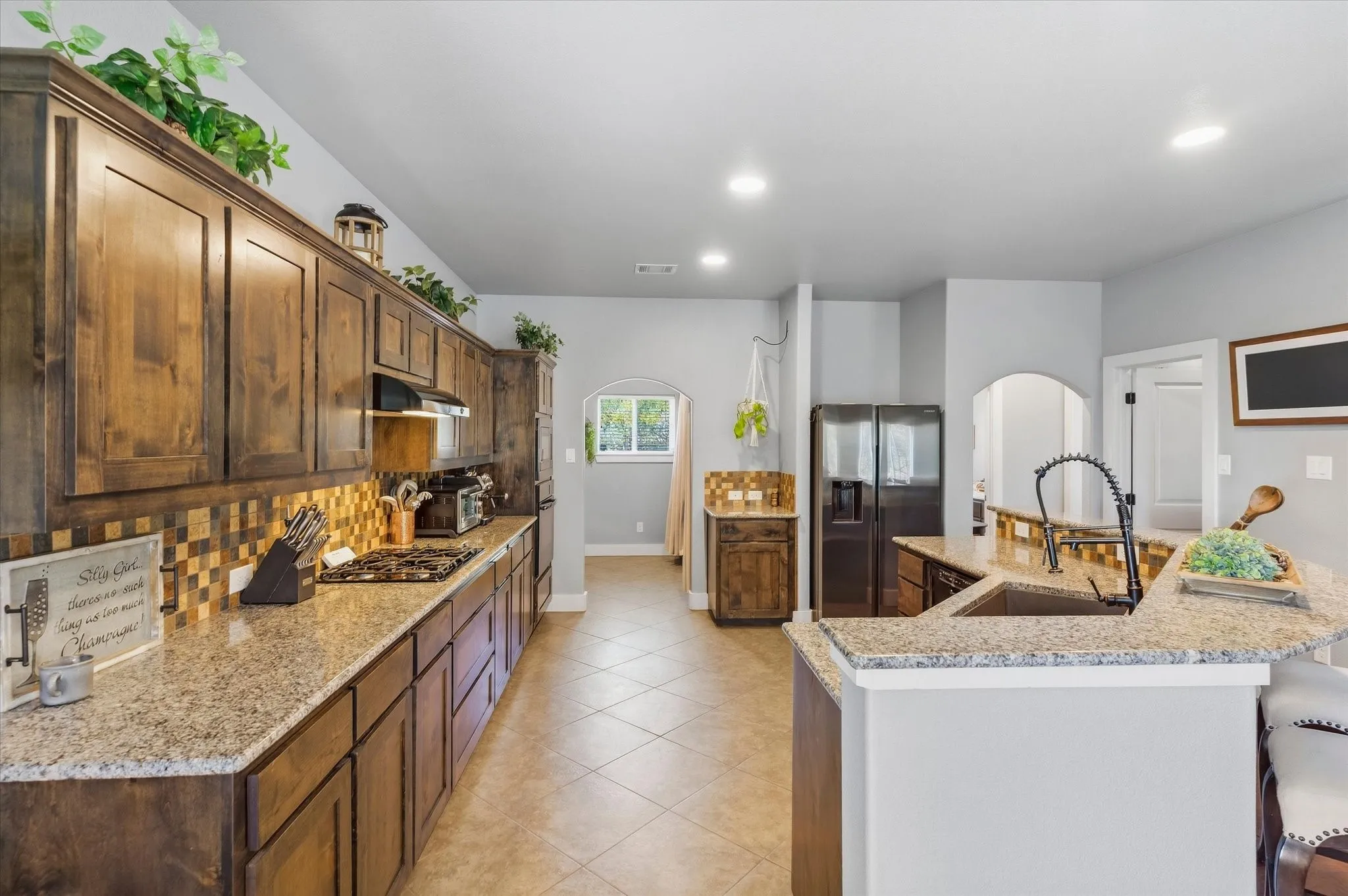 Gourmet kitchen featuring extensive wood cabinetry, granite countertops, tile backsplash, and a large kitchen island with integrated sink