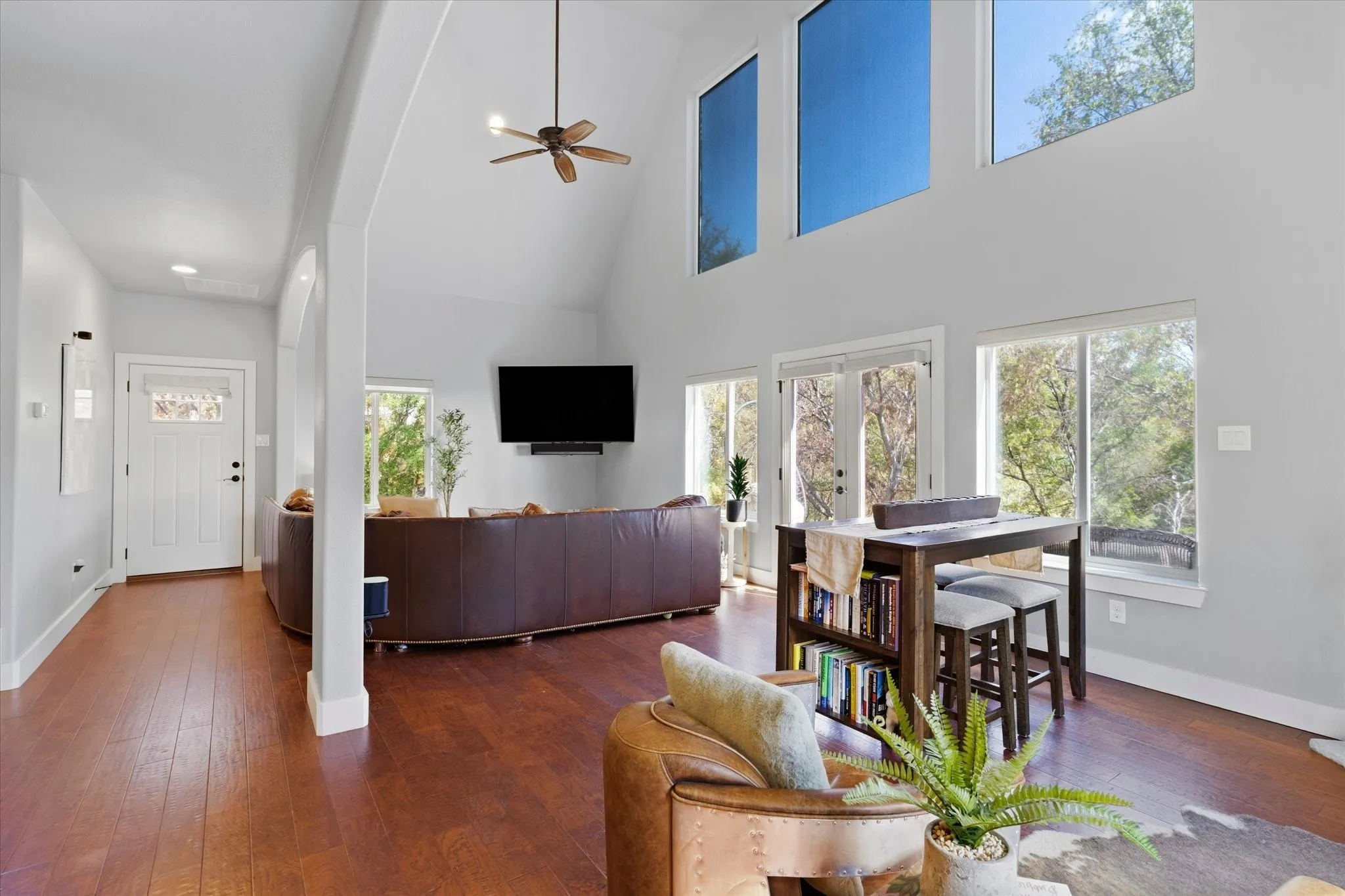 Vaulted ceilings with a ceiling fan, wood-finish flooring, multiple large windows, glass-panel entry door, and recessed lighting
