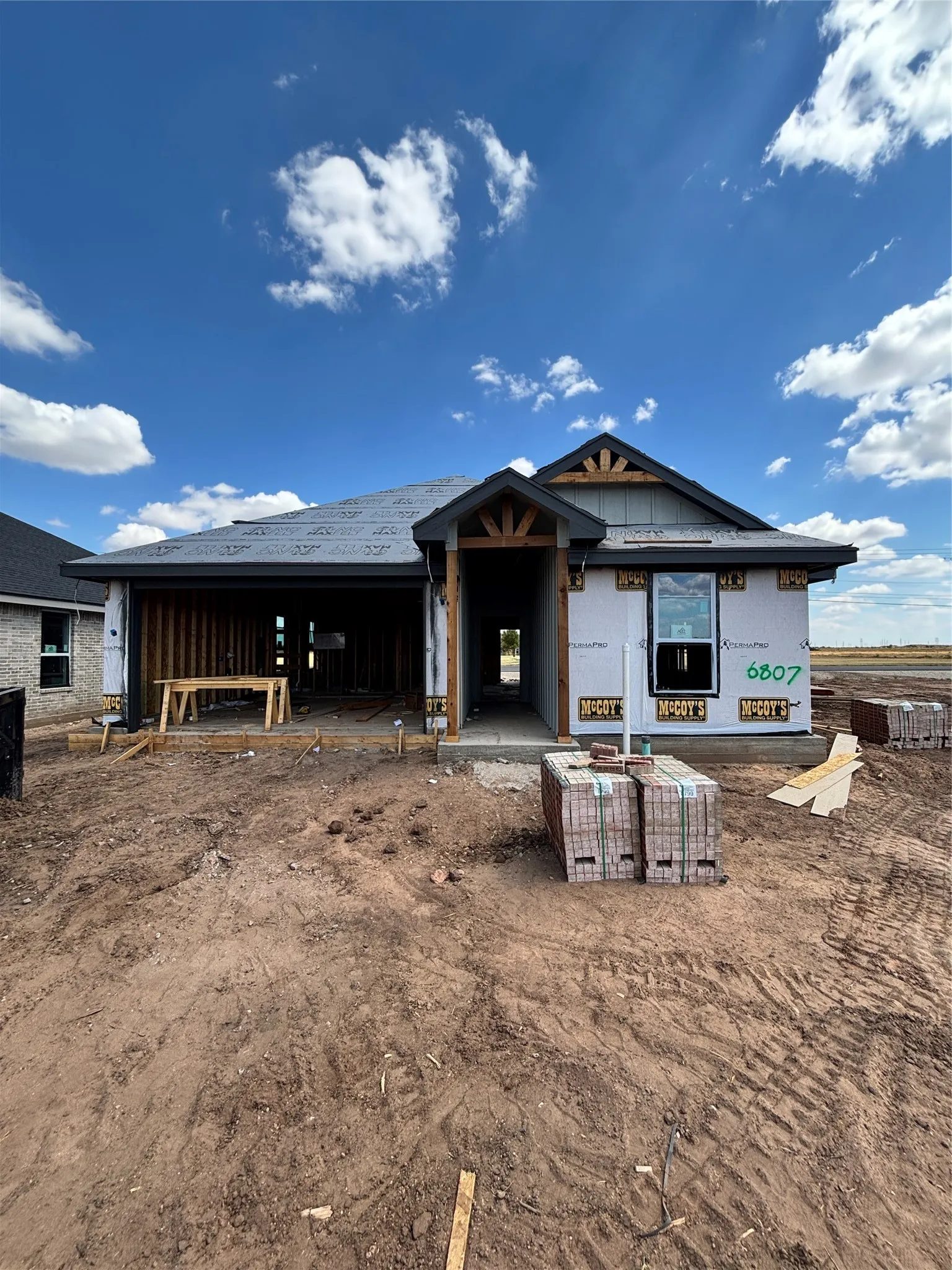 New construction residence featuring a prominent gable roof, exposed wood beam porch entry, and a covered patio area