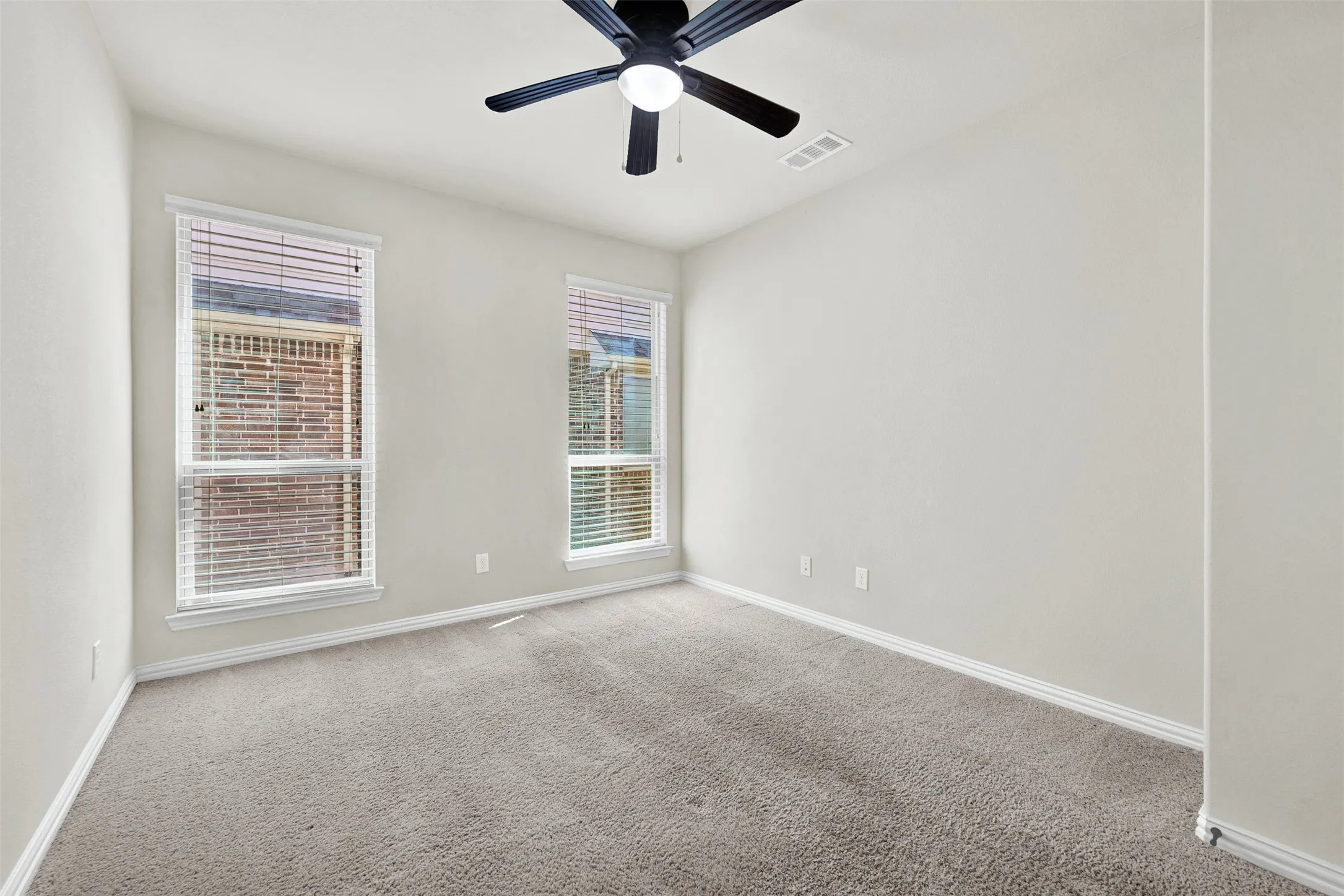 Two windows with blinds, ceiling fan with integrated lighting, and neutral-toned carpeting