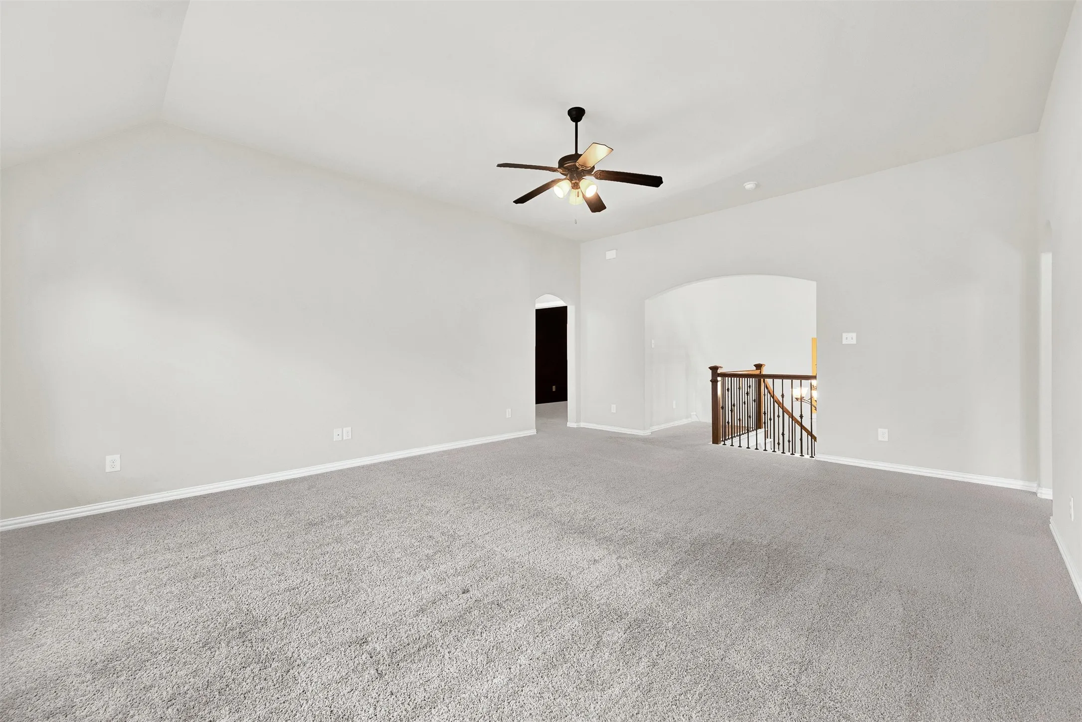 Vaulted ceiling, ceiling fan, carpet flooring, arched doorway, and wood-finish handrail with metal balusters