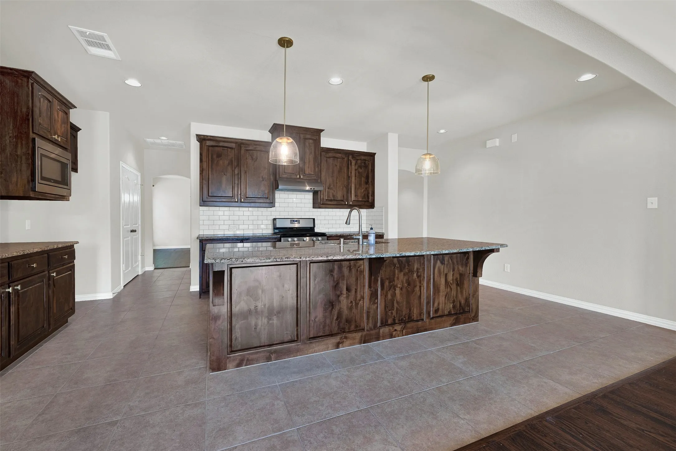 Kitchen featuring dark wood cabinetry, granite countertops, subway tile backsplash, and a large center island with pendant lighting